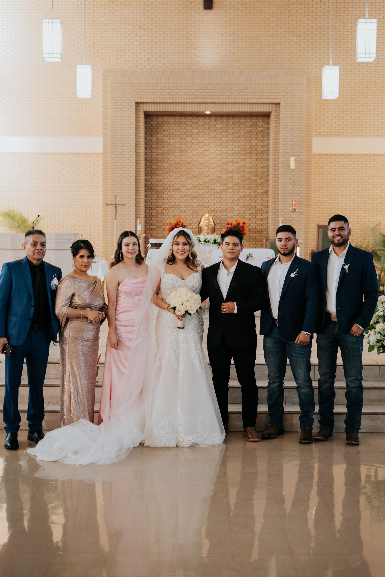 Wedding party members line up against a beige wall wearing formal attire in navy blue and blush pink colors.