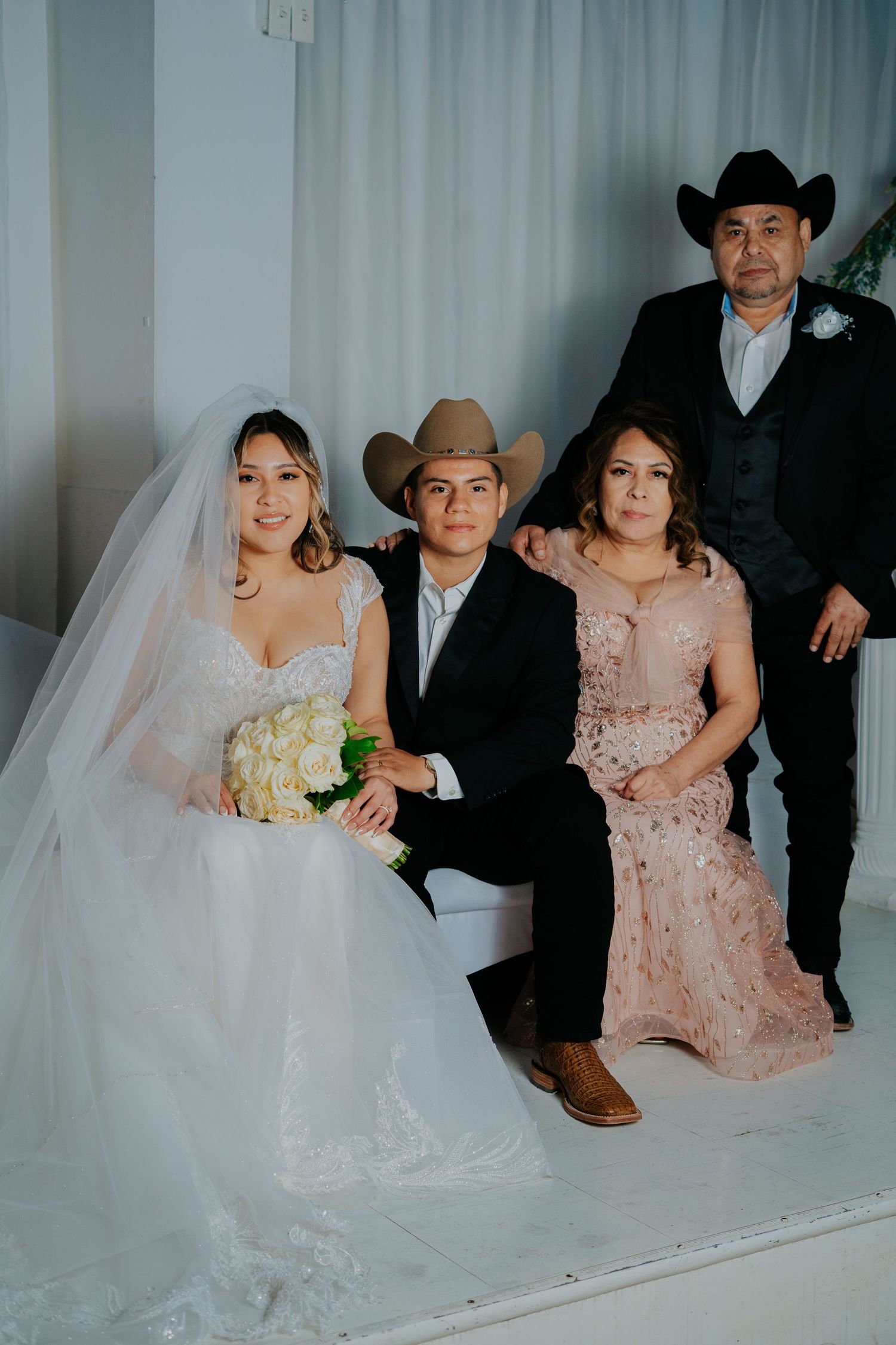 Wedding party poses together in formal attire with bride in white gown and others wearing pink dresses and cowboy hats.