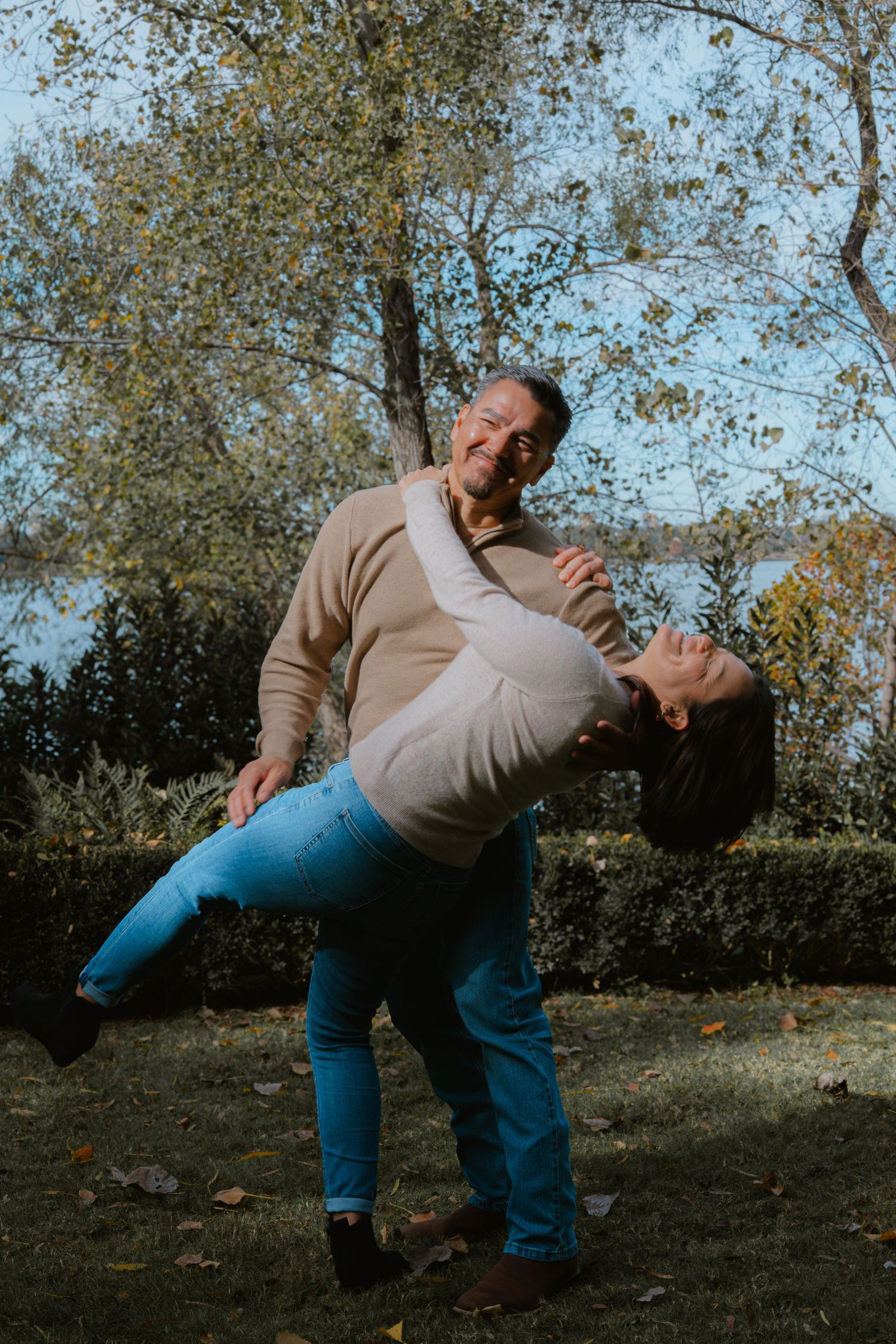 A sequence showing a person in blue jeans and beige sweater playfully falling down on a grassy slope.