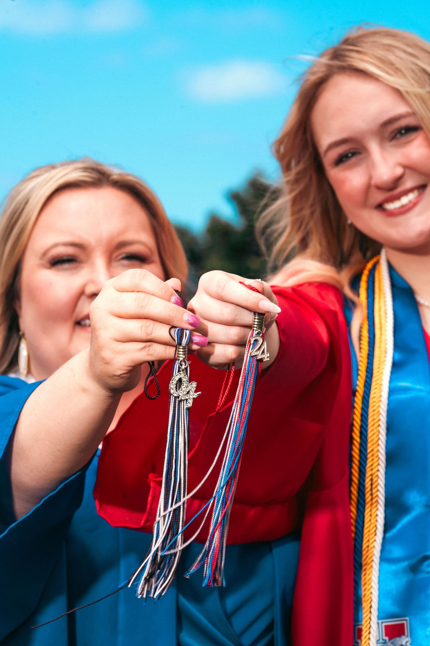 Graduates holding tassels against bright blue sky showing their academic achievements.