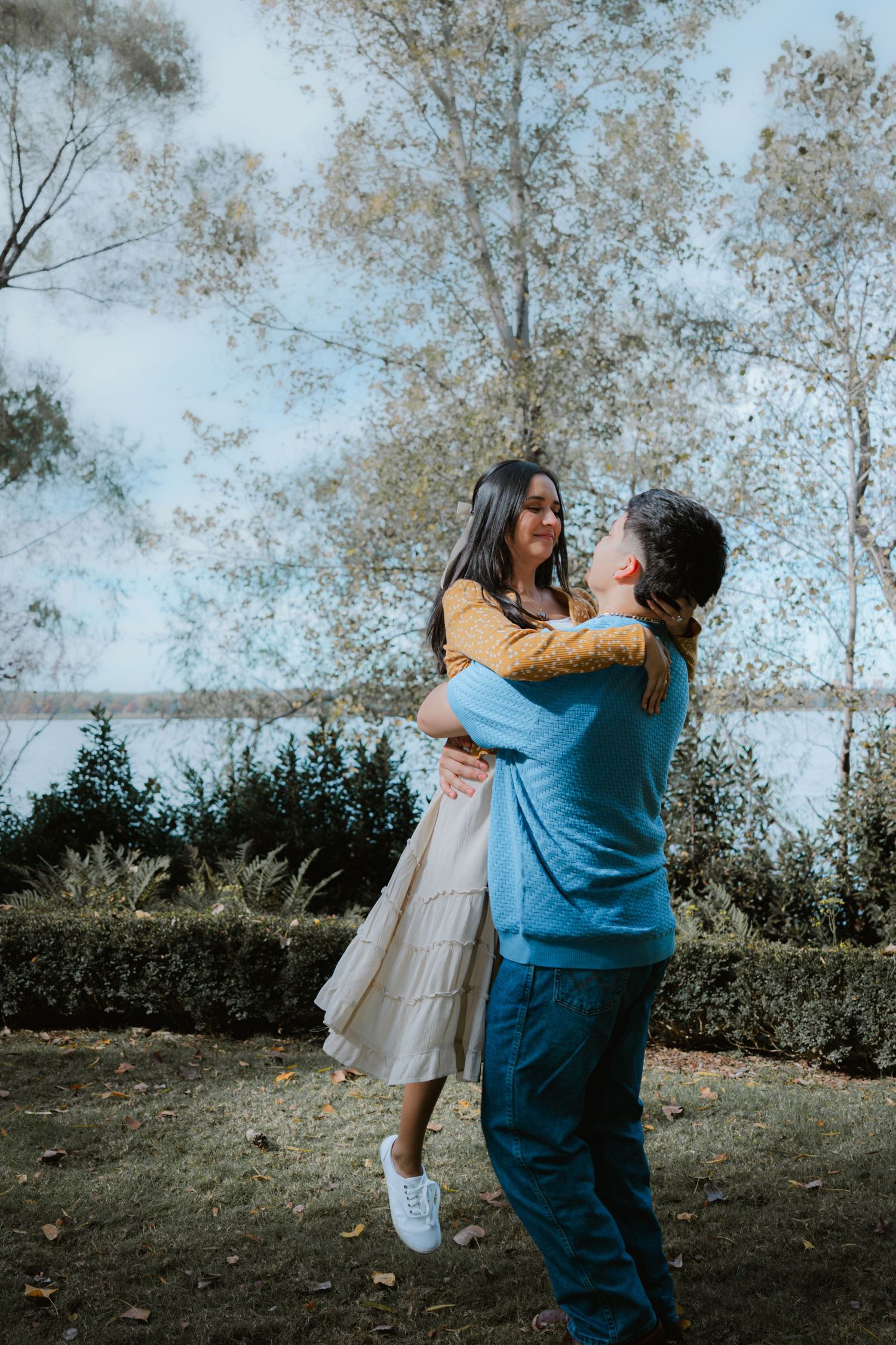 A couple embraces playfully outdoors with trees and natural scenery in the background.