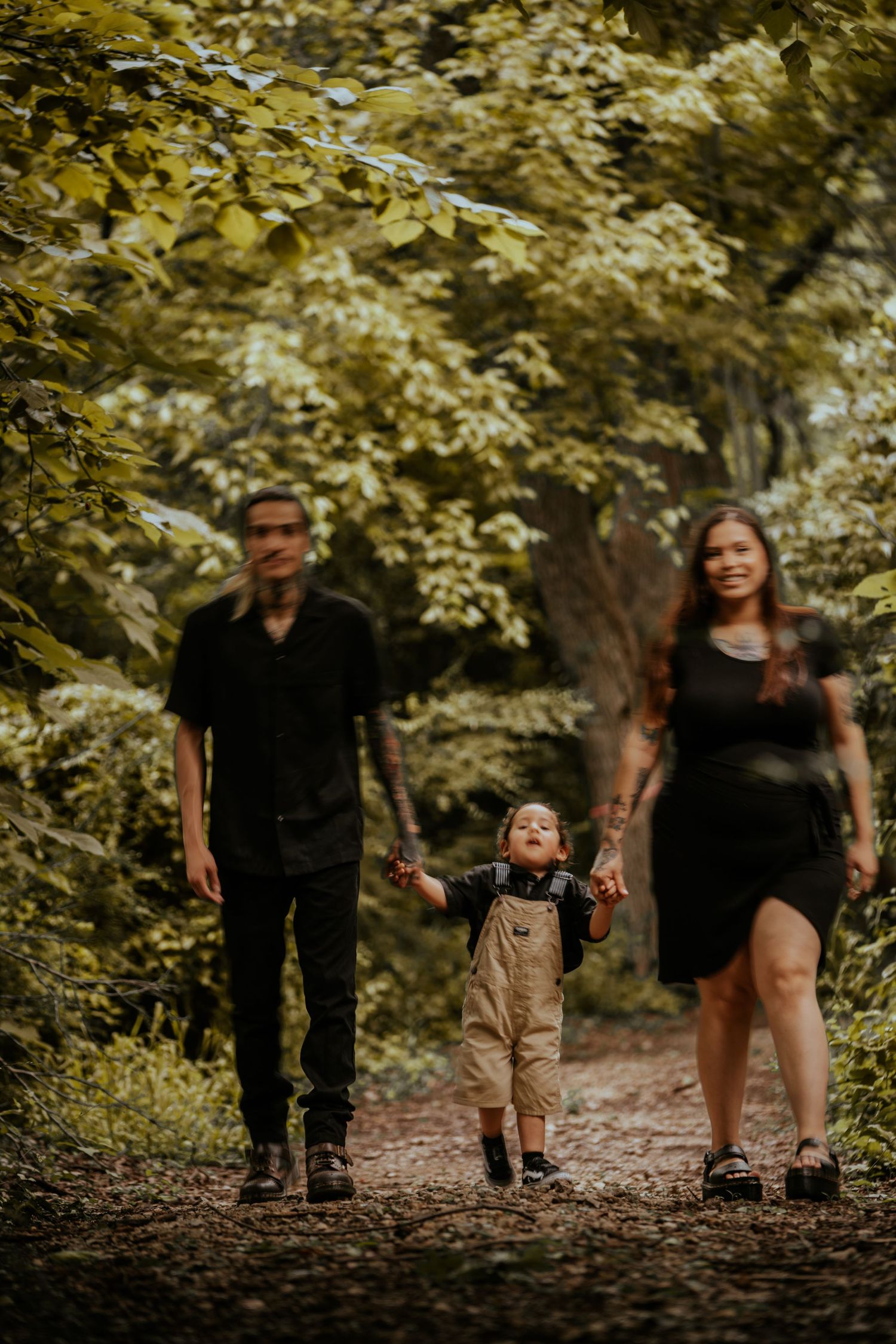 A family walks together on a wooded path surrounded by golden autumn foliage.