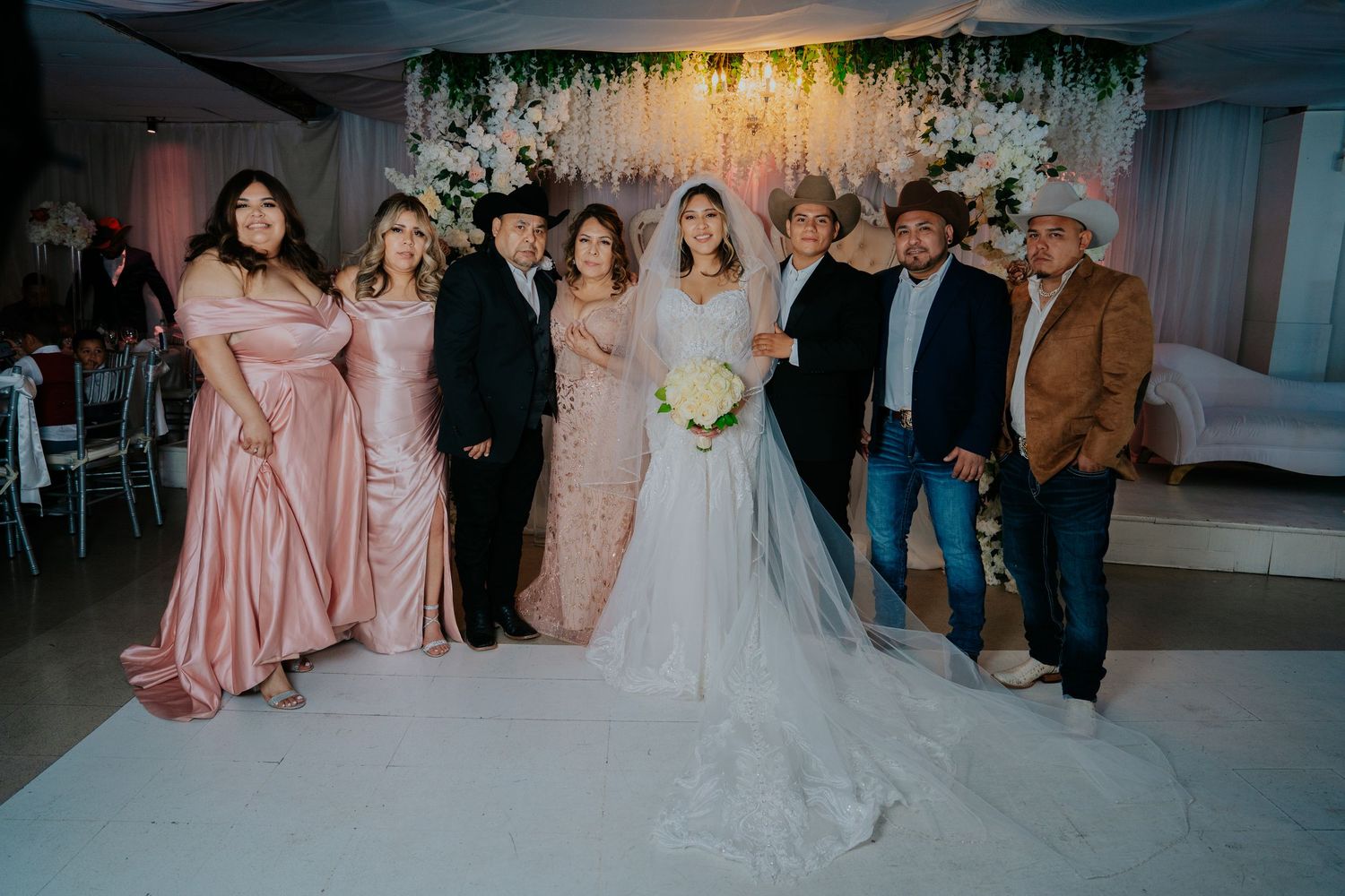 Wedding party members pose together in formal attire at an elegant indoor reception venue.