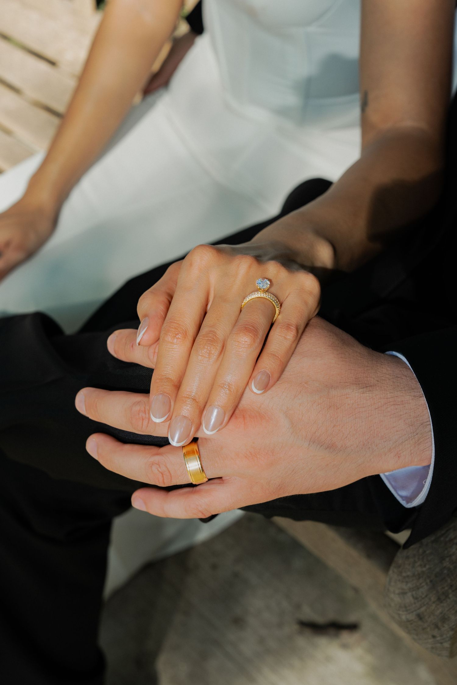 Newlywed couple displaying wedding rings, bride wearing diamond engagement ring and groom wearing gold band, hands together.