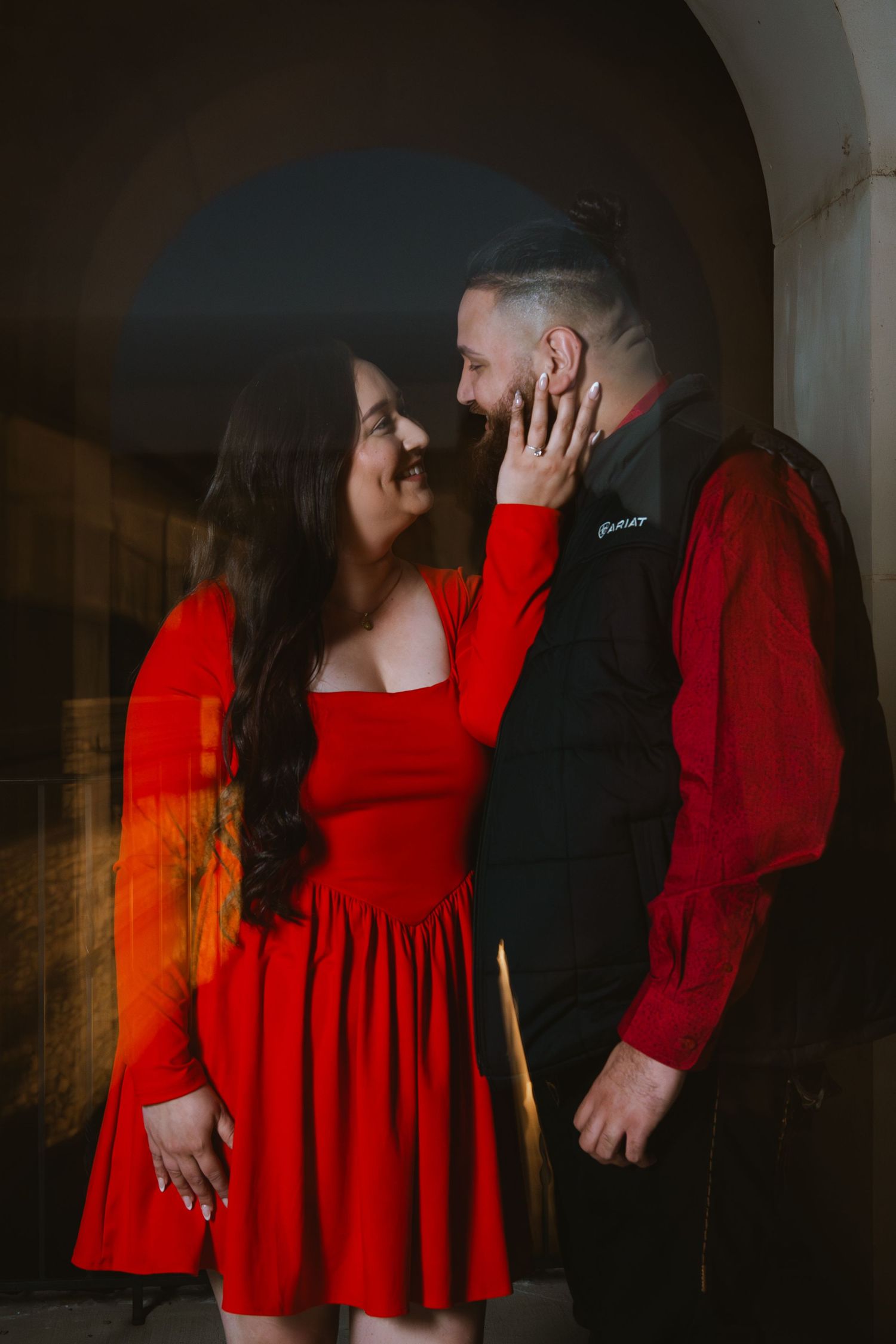 Couple in matching red and black outfits sharing a tender moment under an archway.