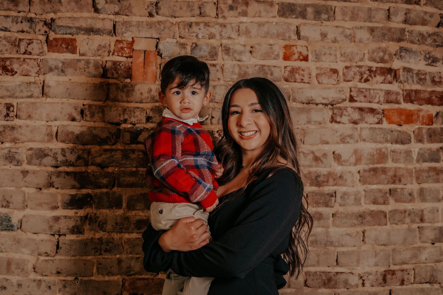 Family poses together against rustic brick wall background in warm toned lifestyle photography session.