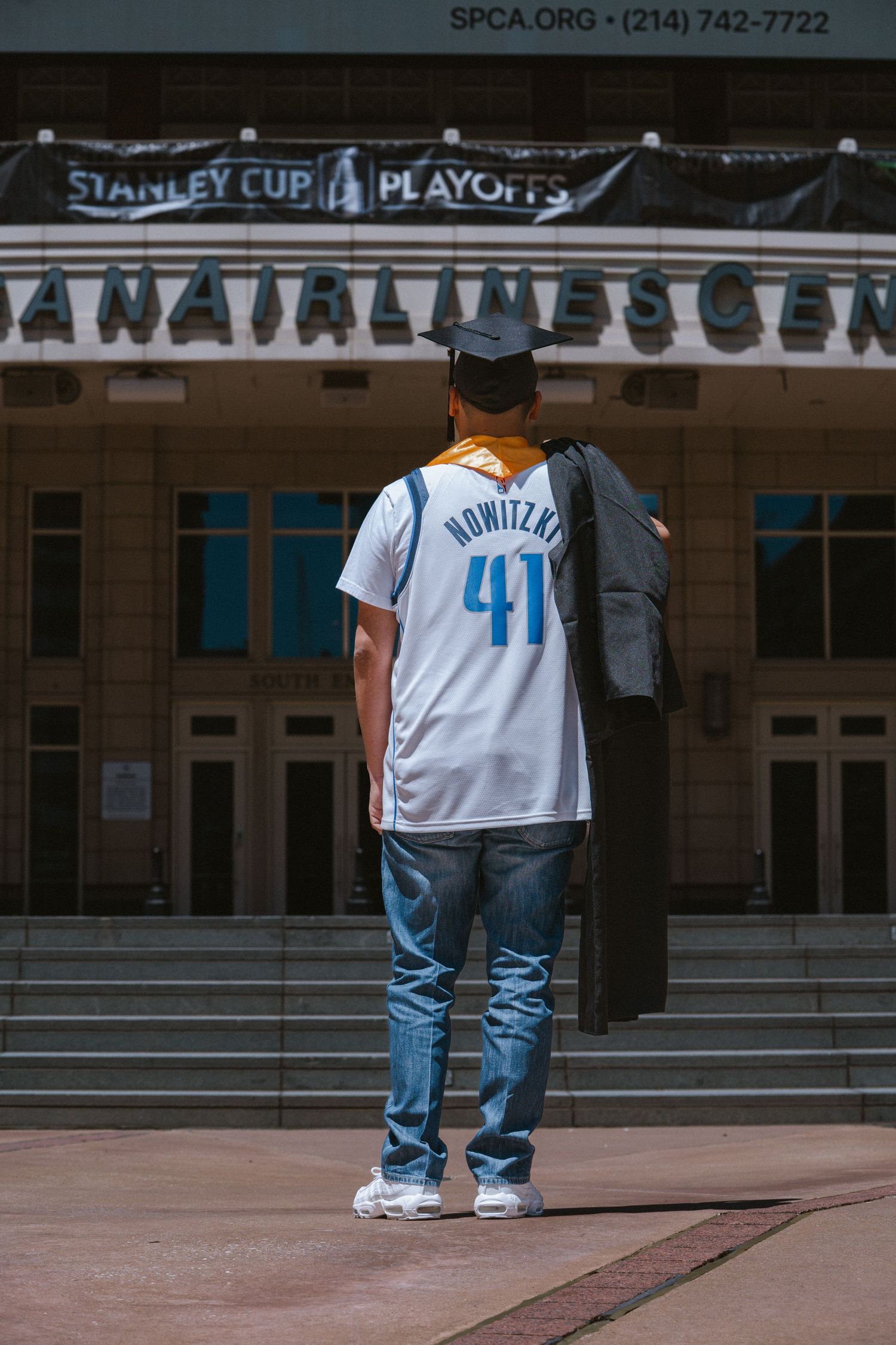 Graduate in Nowitzki 41 jersey and cap stands before American Airlines Center during Stanley Cup Playoffs.