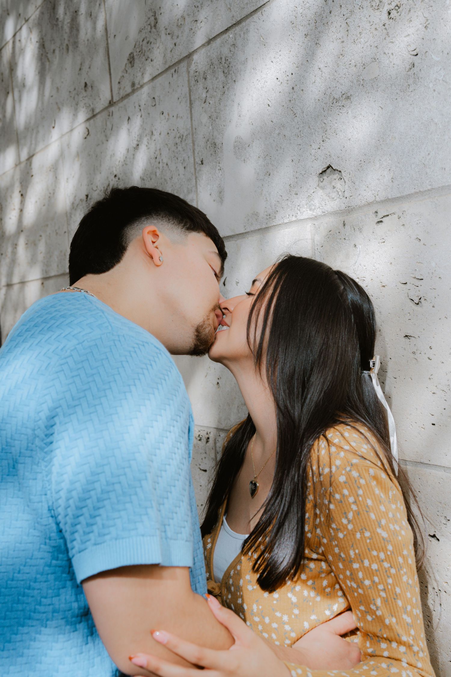 A romantic moment captured against a concrete wall with two people in blue and yellow polka dot outfits.