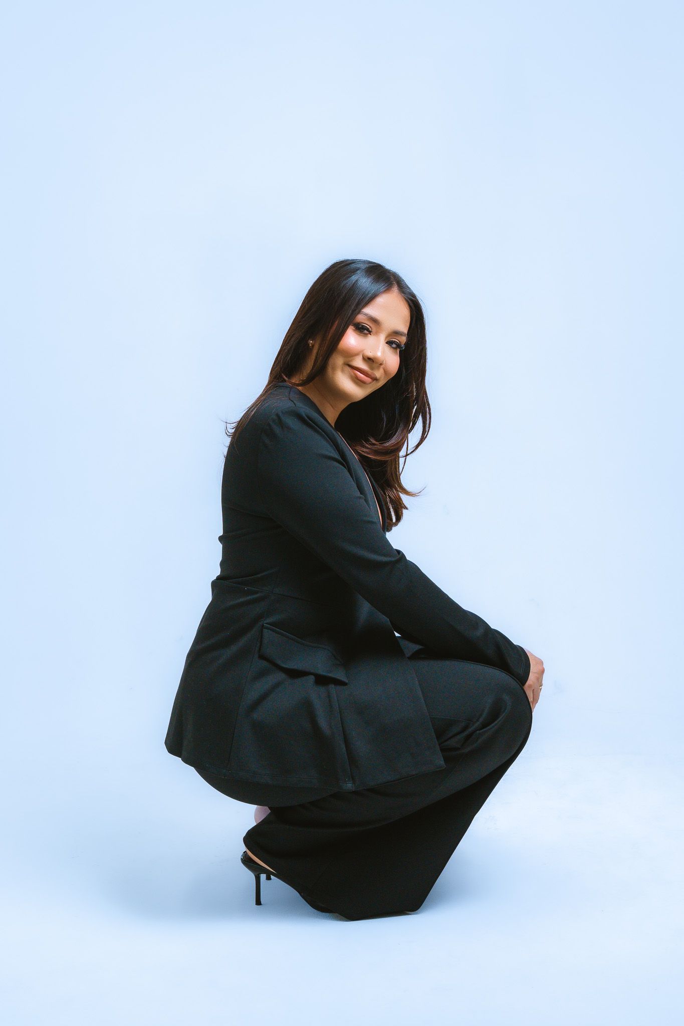 Person in all black attire sits in contemplative poses against white background in artistic photo series.