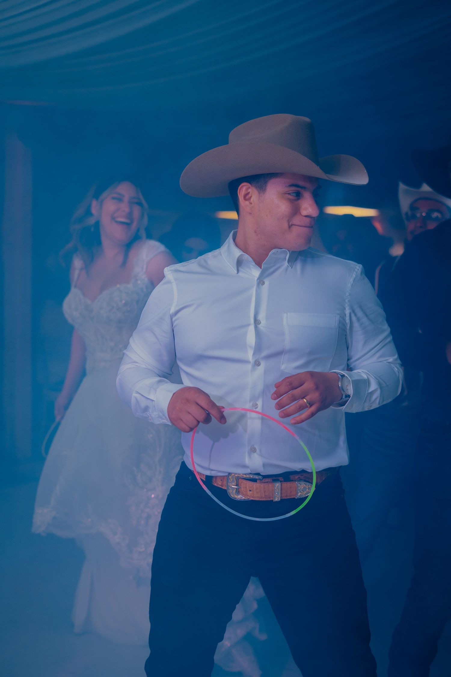 A couple in western attire dance together at an event with blue lighting and atmospheric effects in the background.
