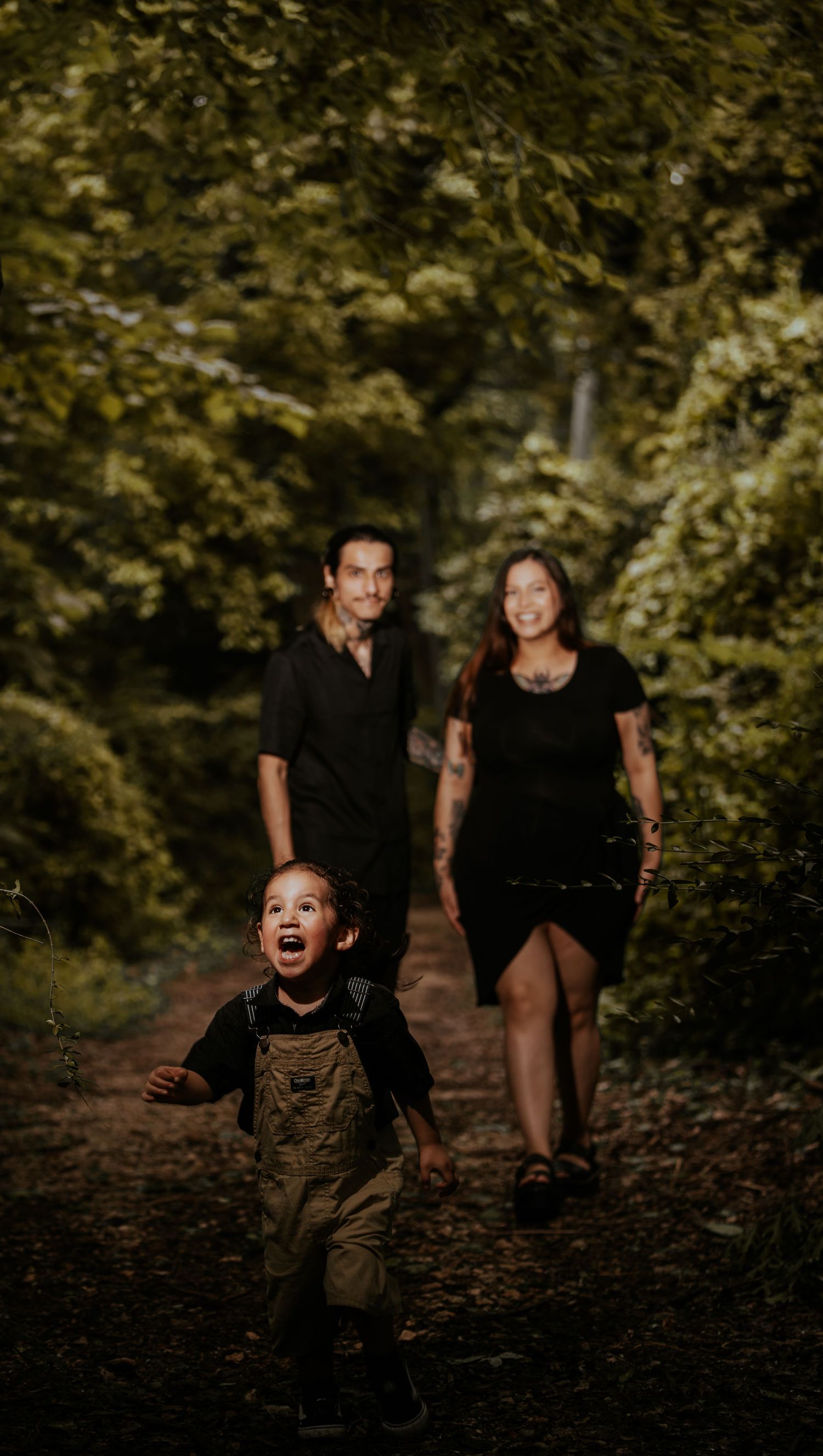 A child in brown overalls runs joyfully through a wooded path on an autumn day.