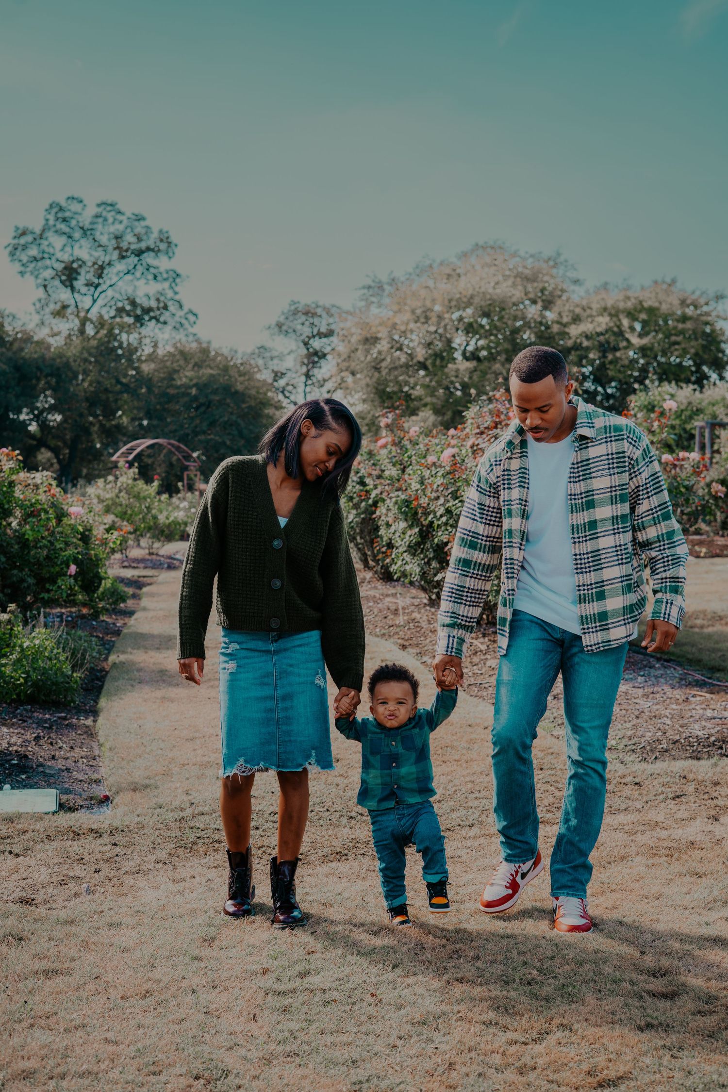 Family members in coordinated blue outfits walk together on a dirt path with flowering trees in the background.