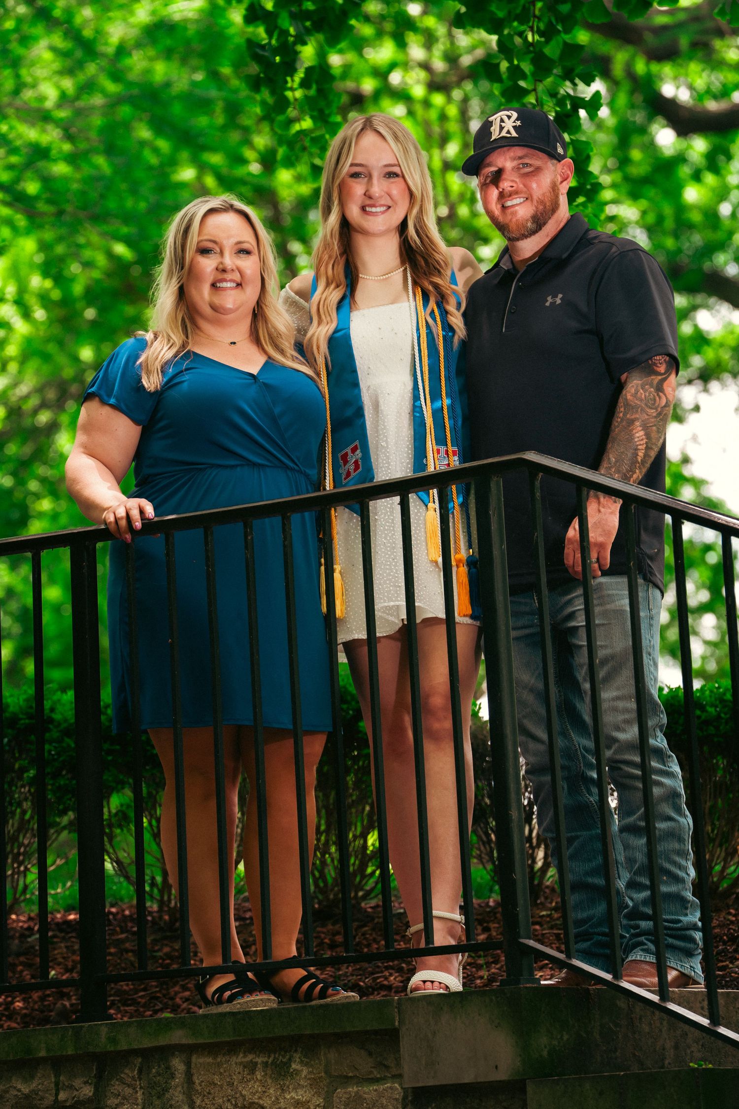A group poses together on an outdoor deck surrounded by lush green trees and foliage in summer.