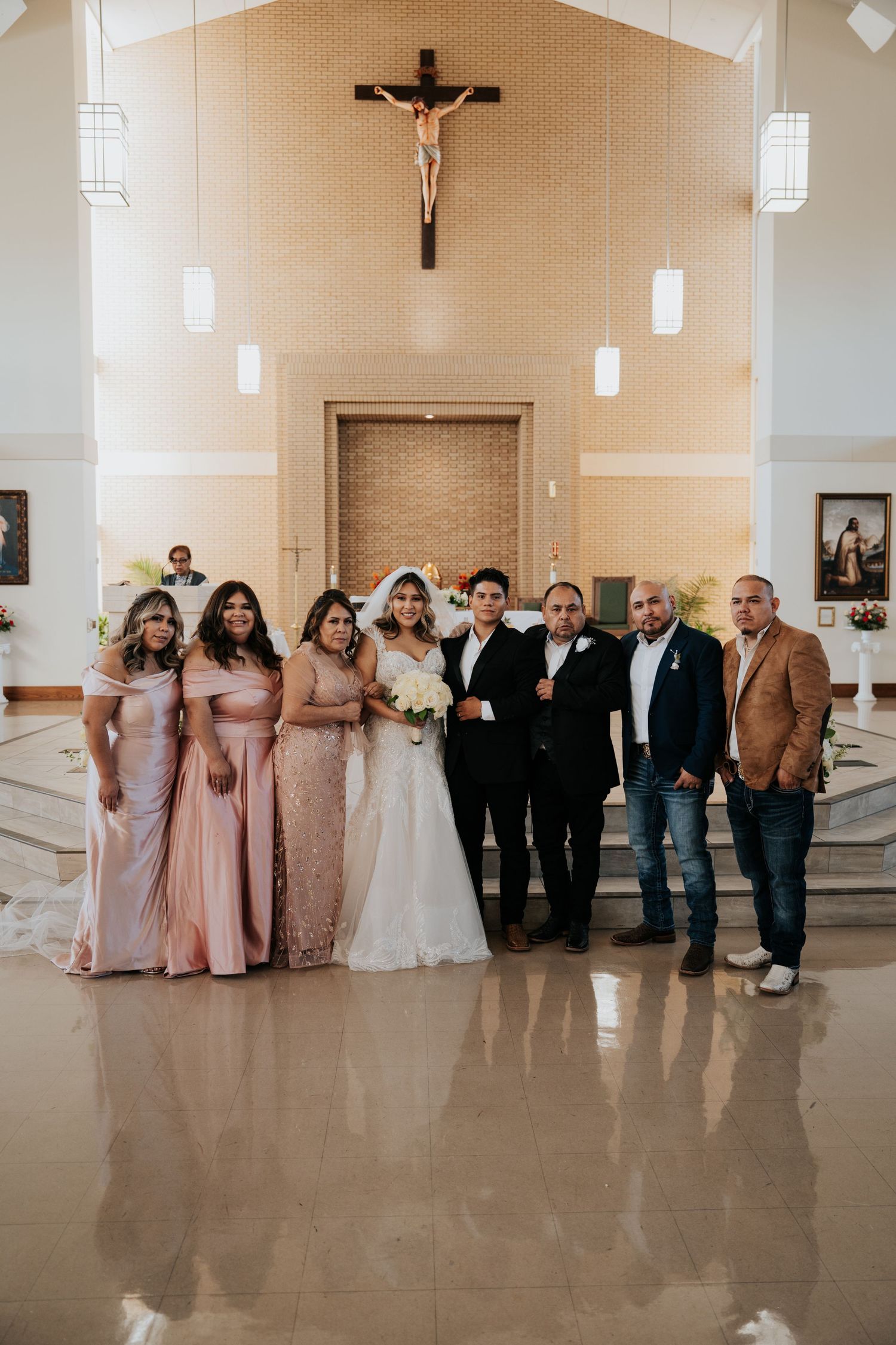 Wedding party poses together in a church interior with bridesmaids in pink dresses and groomsmen in dark suits.