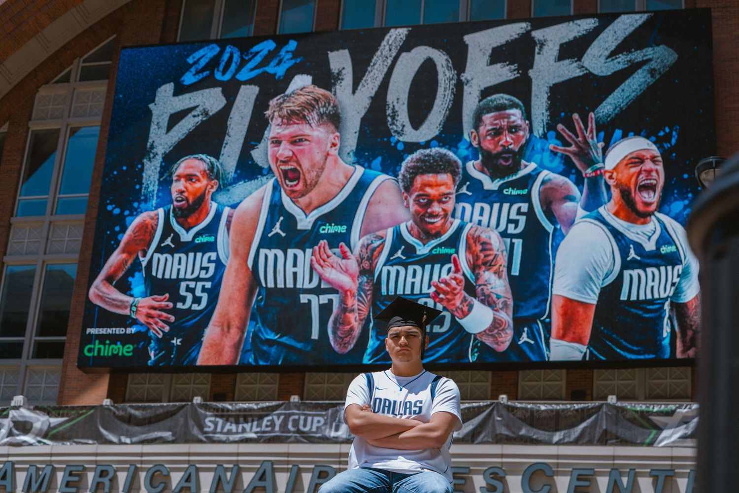 Fan poses in front of 2024 NBA Playoffs Dallas Mavericks billboard featuring players including Luka Doncic.