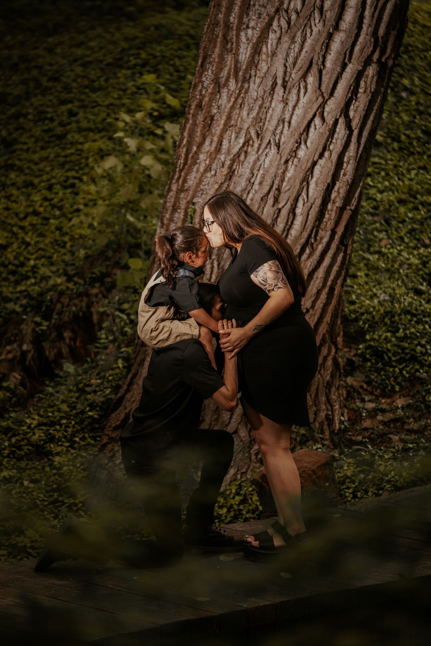 A figure crouches near a large tree trunk in a dark forest setting, creating a mysterious and moody atmosphere.