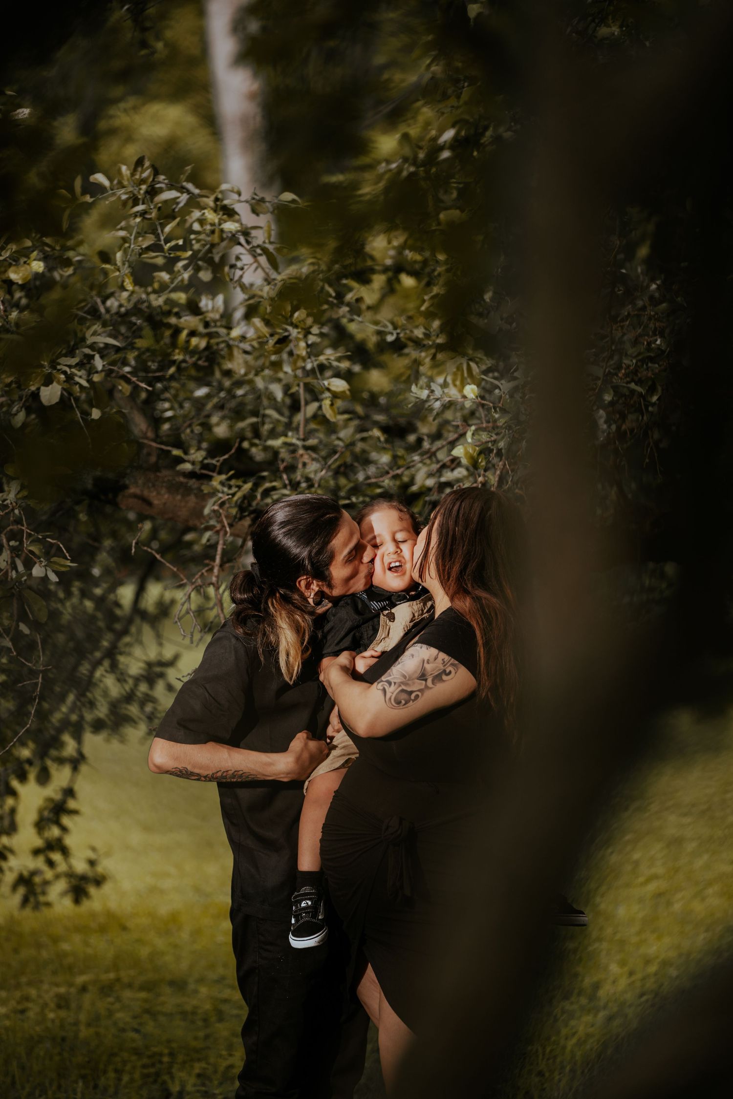 A romantic moment captured through tree branches in a natural outdoor setting.