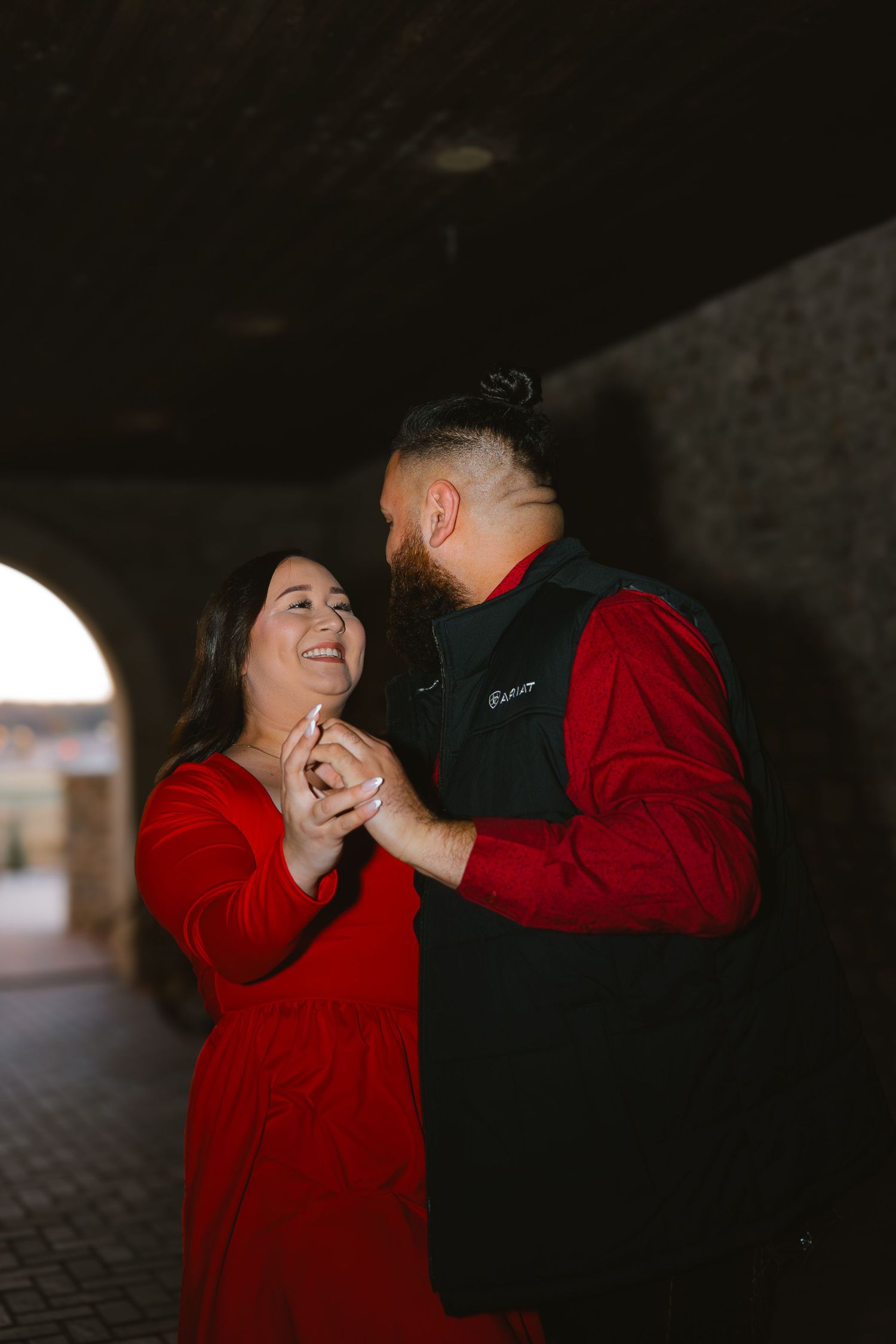 Couple in matching red outfits dancing romantically under a dark archway, smiling at each other.