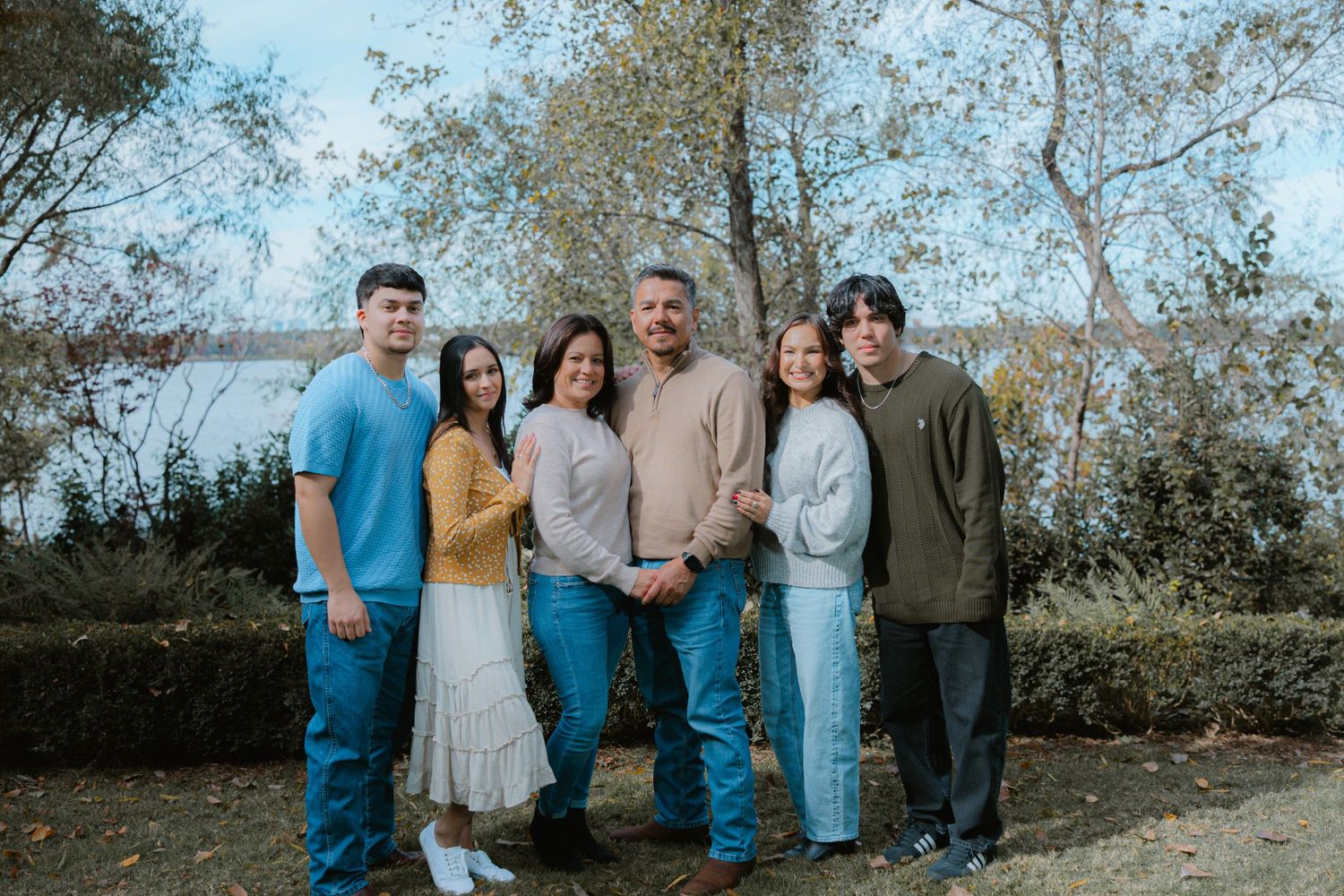 A group of people wearing casual attire pose together outdoors against a backdrop of autumn trees and foliage.