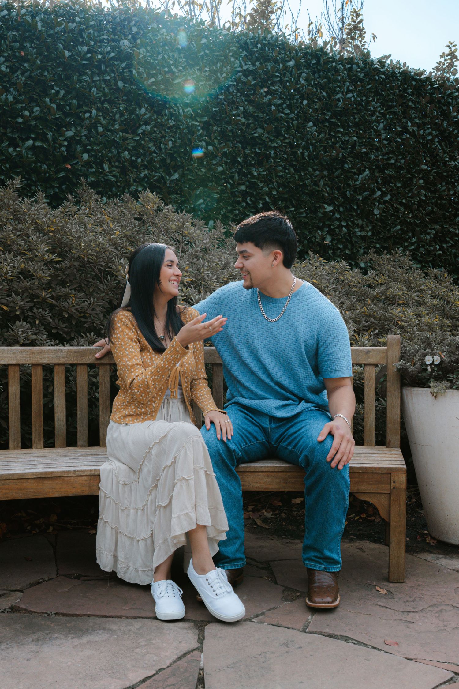 Couple sitting together on an outdoor wooden bench sharing a sweet moment in a garden setting.