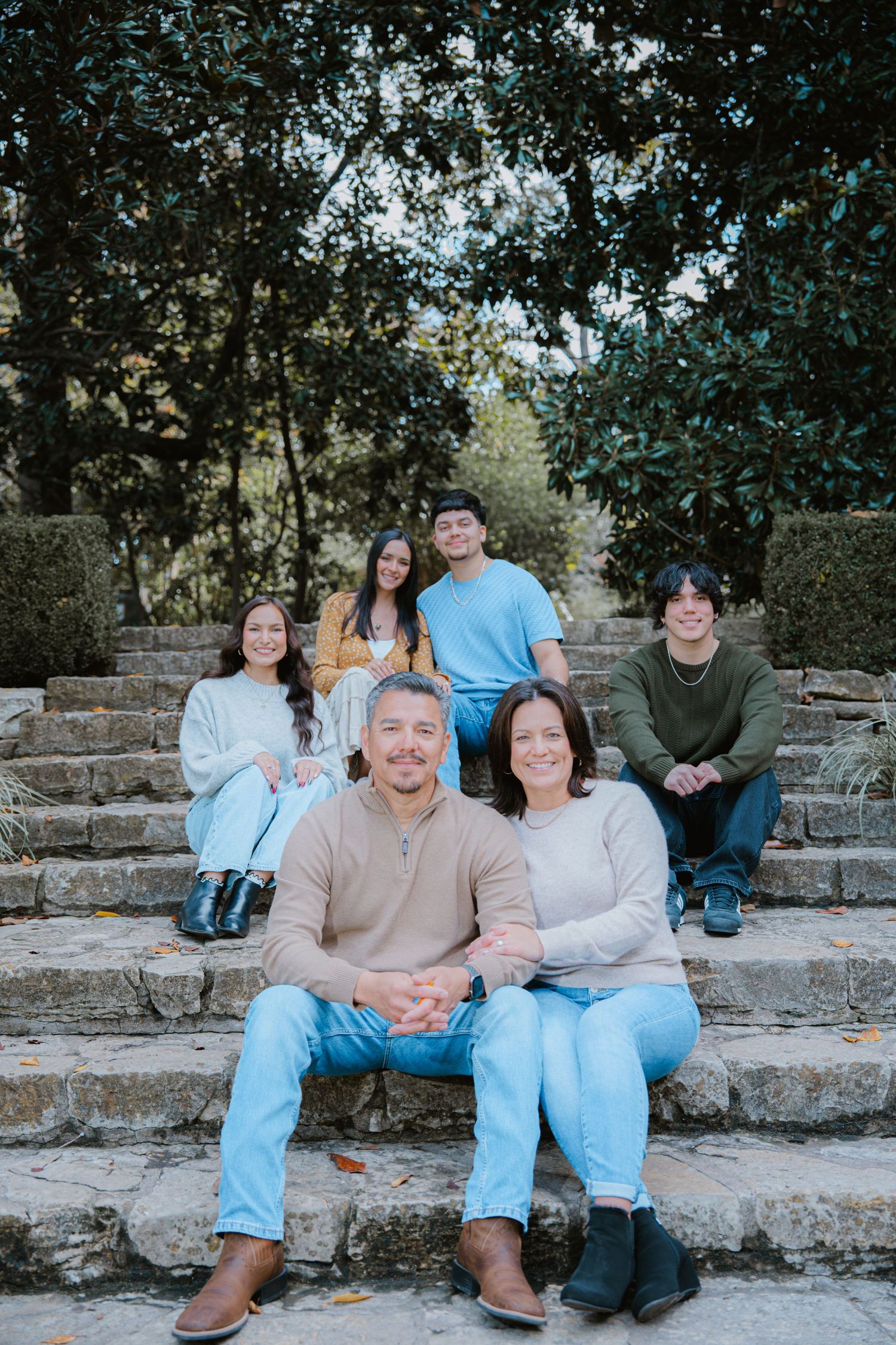 A group sits casually on stone steps outdoors surrounded by trees and greenery.