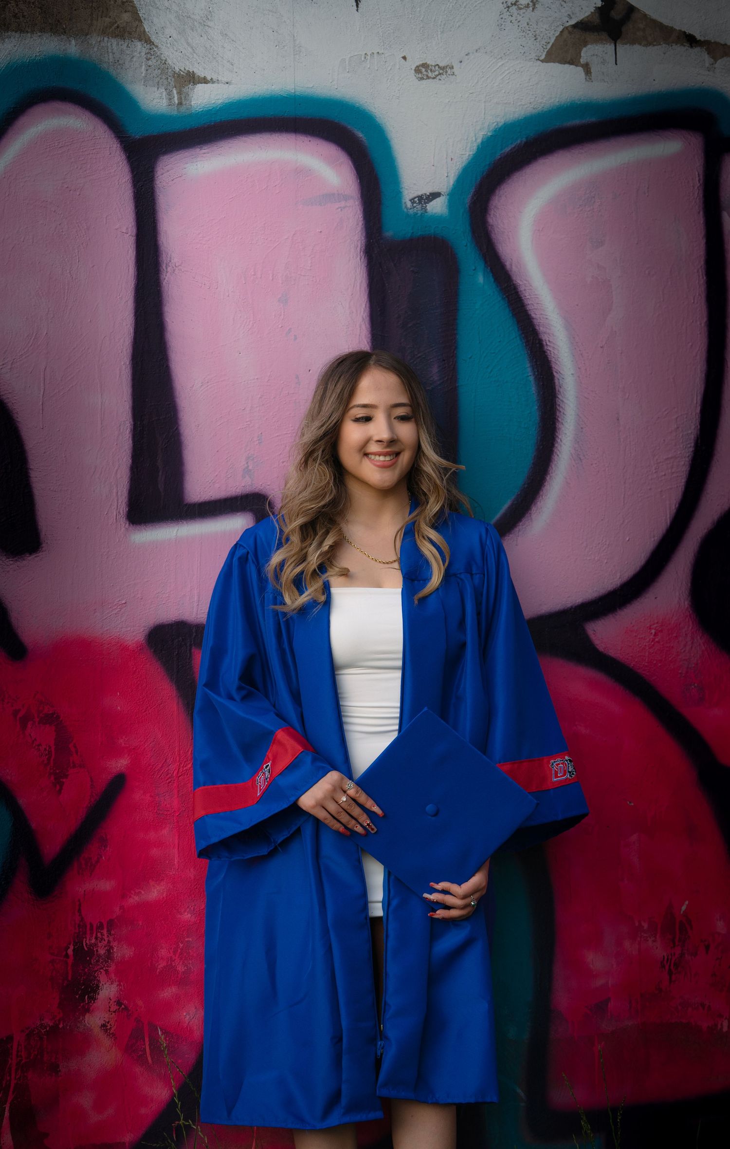 A person wearing a bright royal blue blazer poses against a graffiti wall with pink and black artwork.