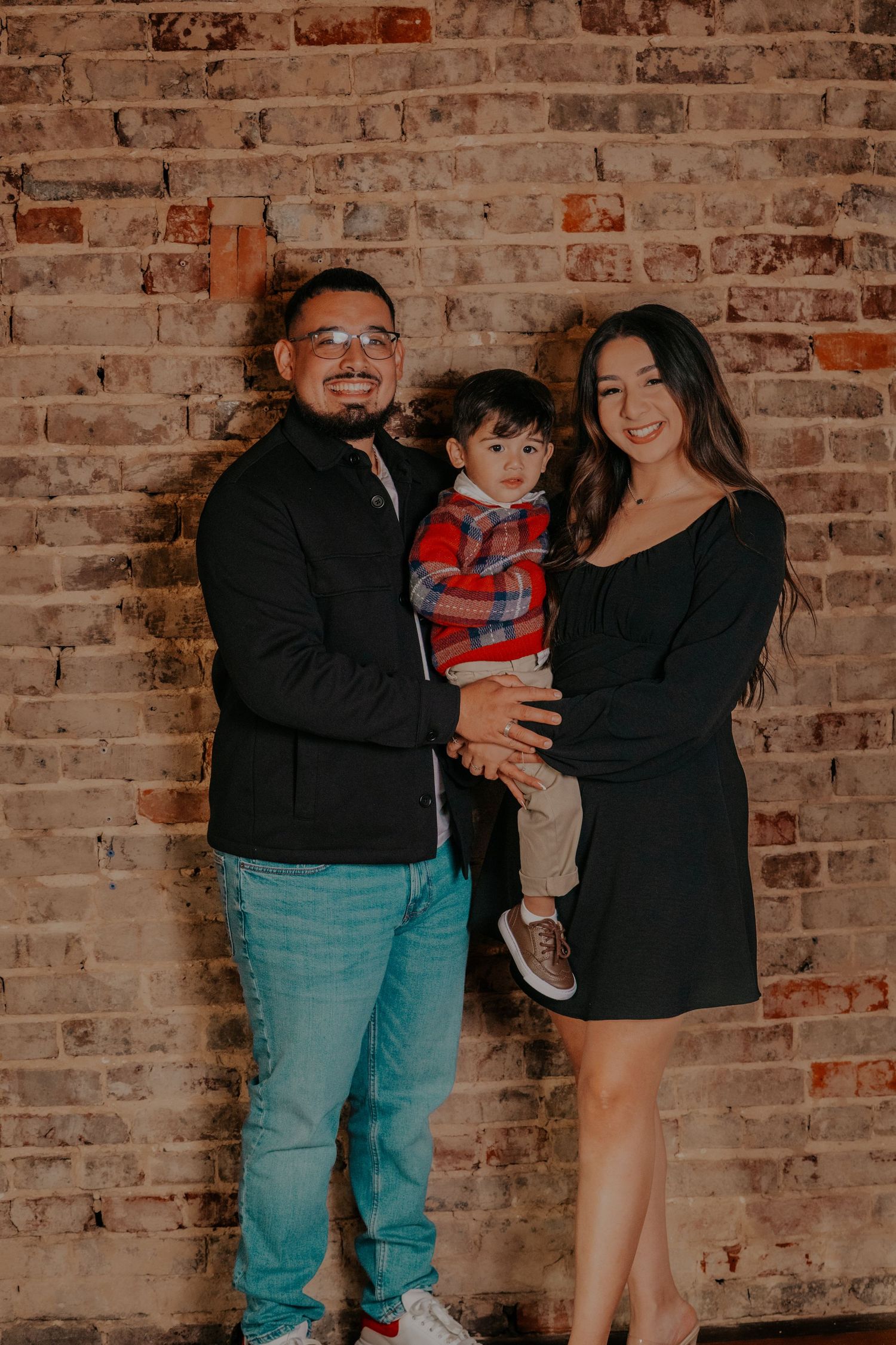 Family holiday portrait session against exposed brick wall with decorative nutcrackers in background.