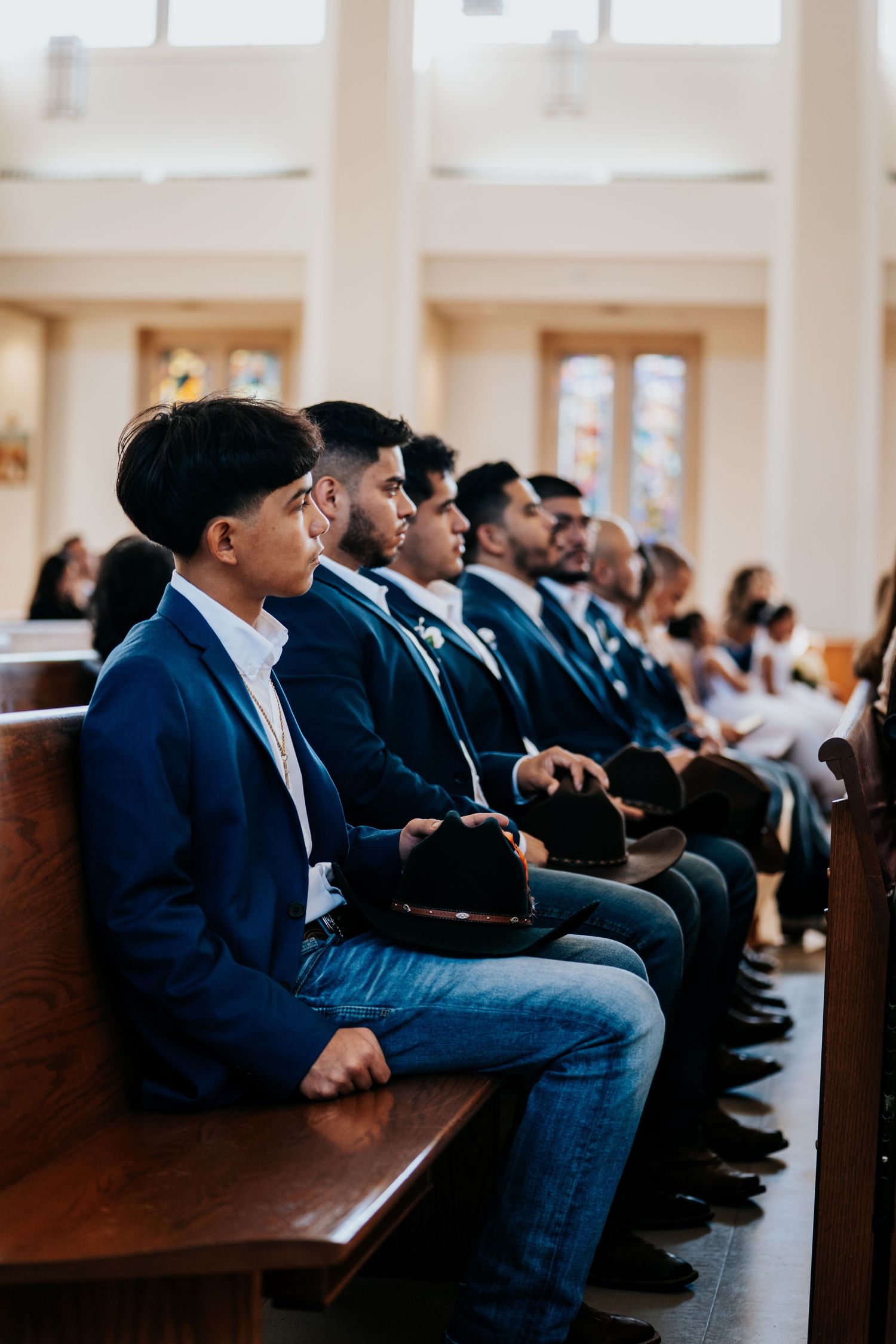 Row of people in navy suits sitting on wooden church pews during a formal ceremony.