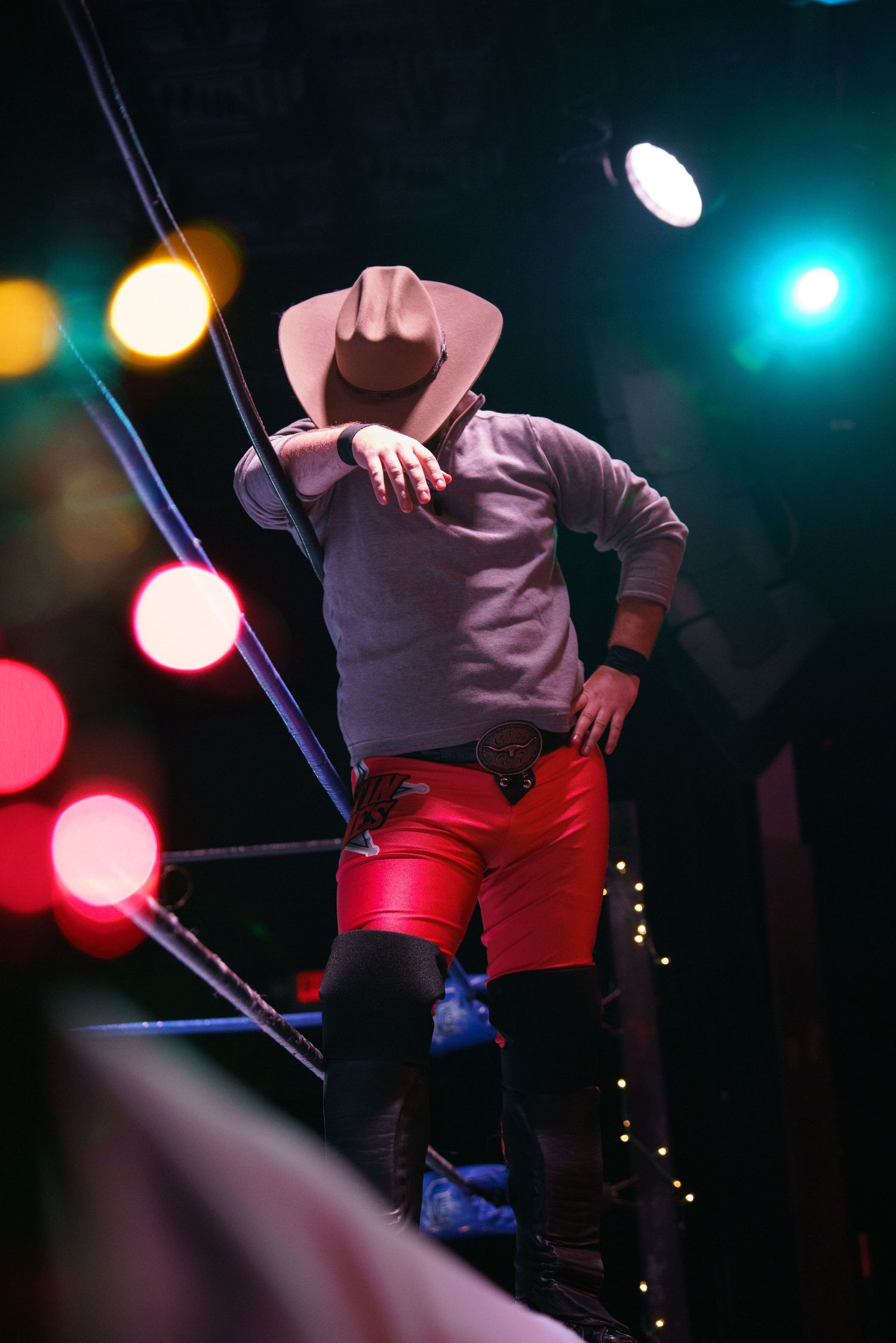 Performer on stage wearing red pants and light colored top under dramatic colored stage lighting.