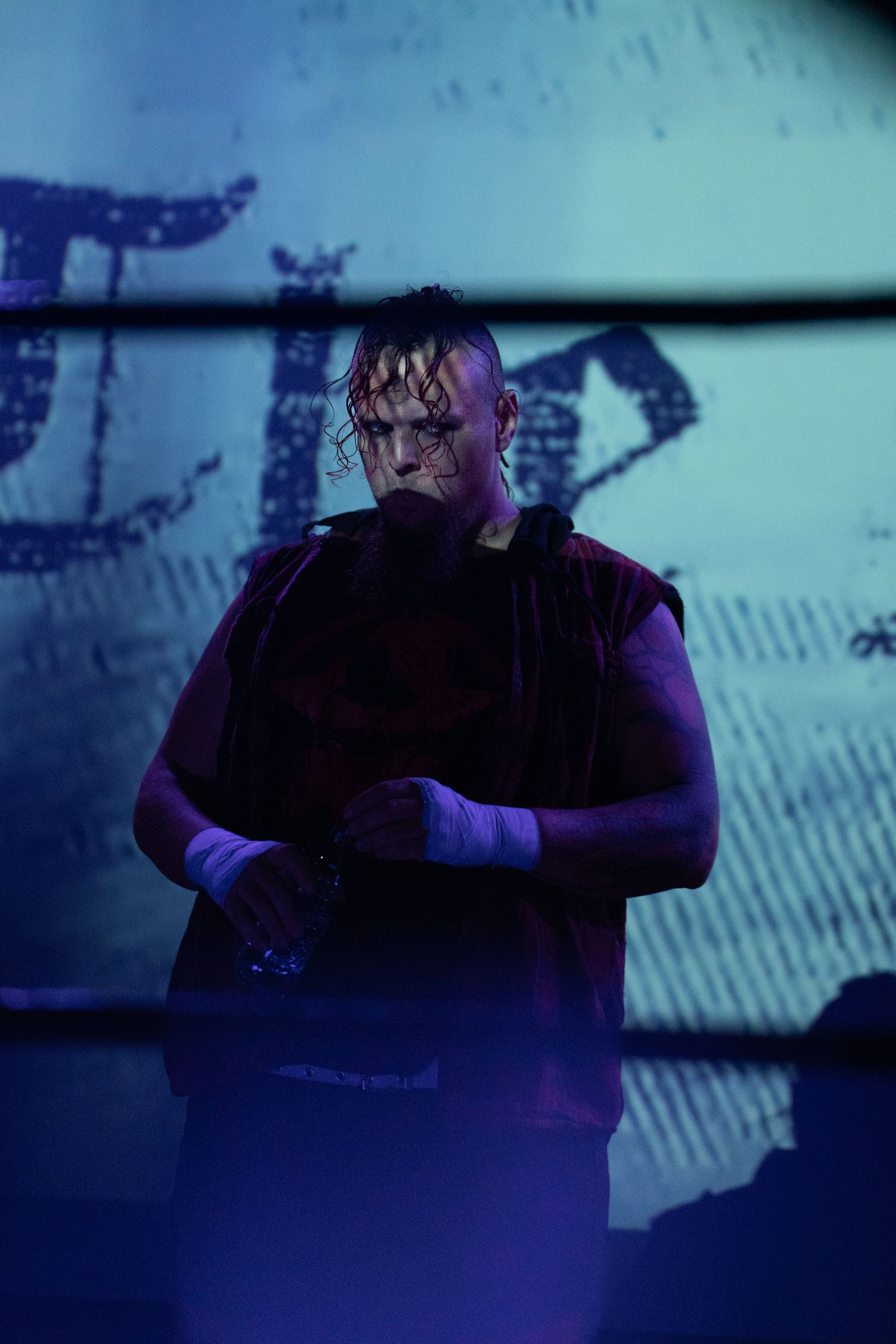 Dark atmospheric portrait shot in blue lighting creates moody professional wrestling ambiance.