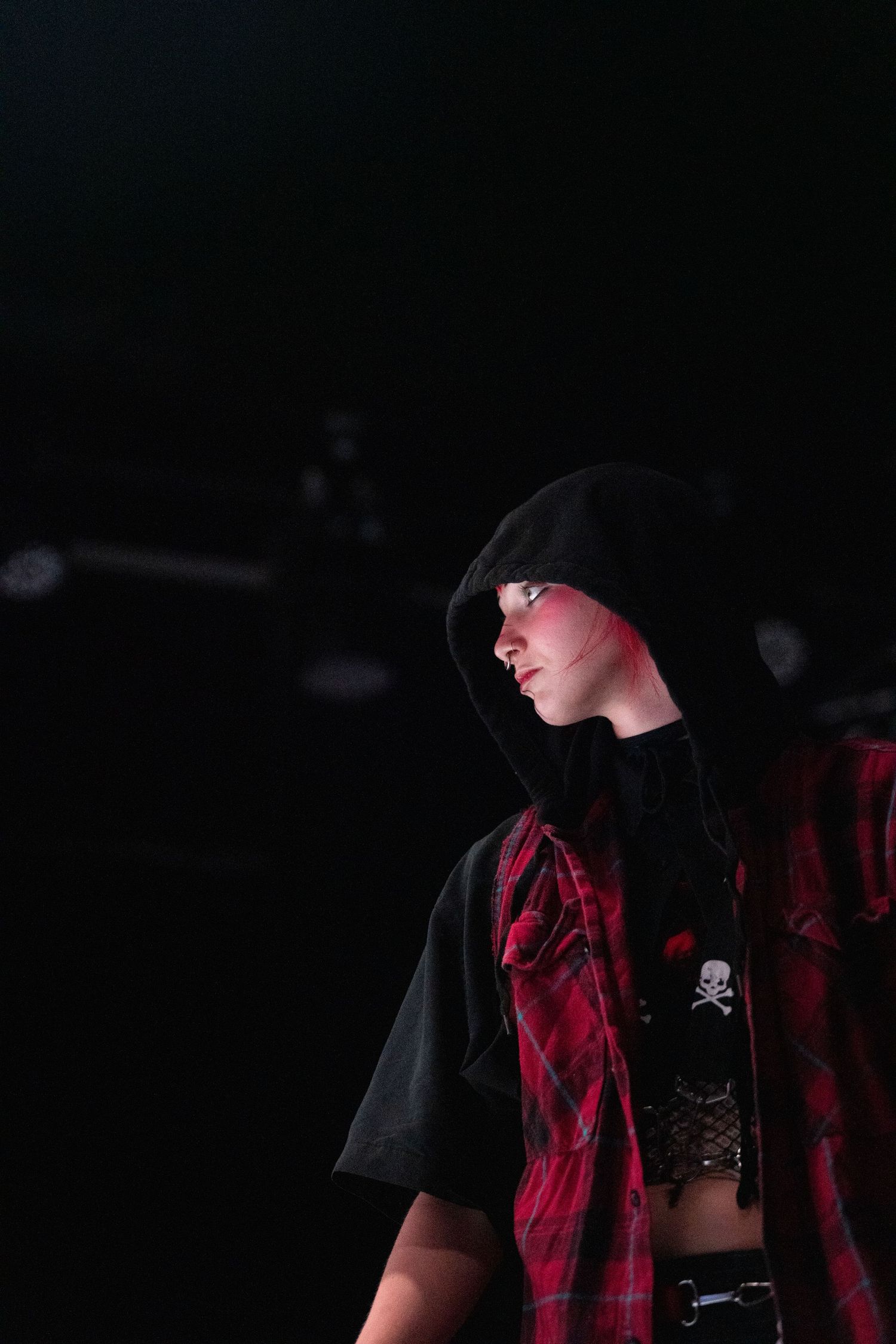 Professional wrestler in dark attire with red lighting performing in a wrestling ring.