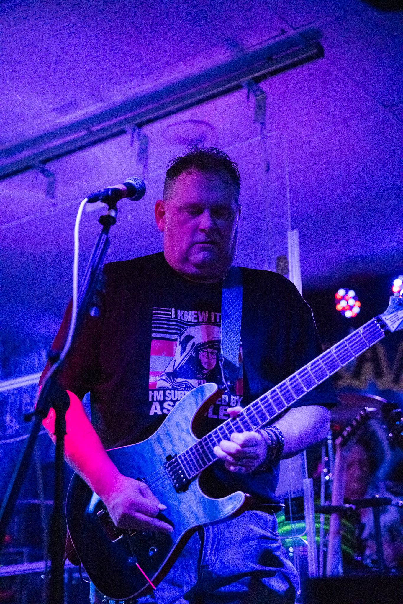 Guitarist performs on stage with purple lighting effects in a club setting.