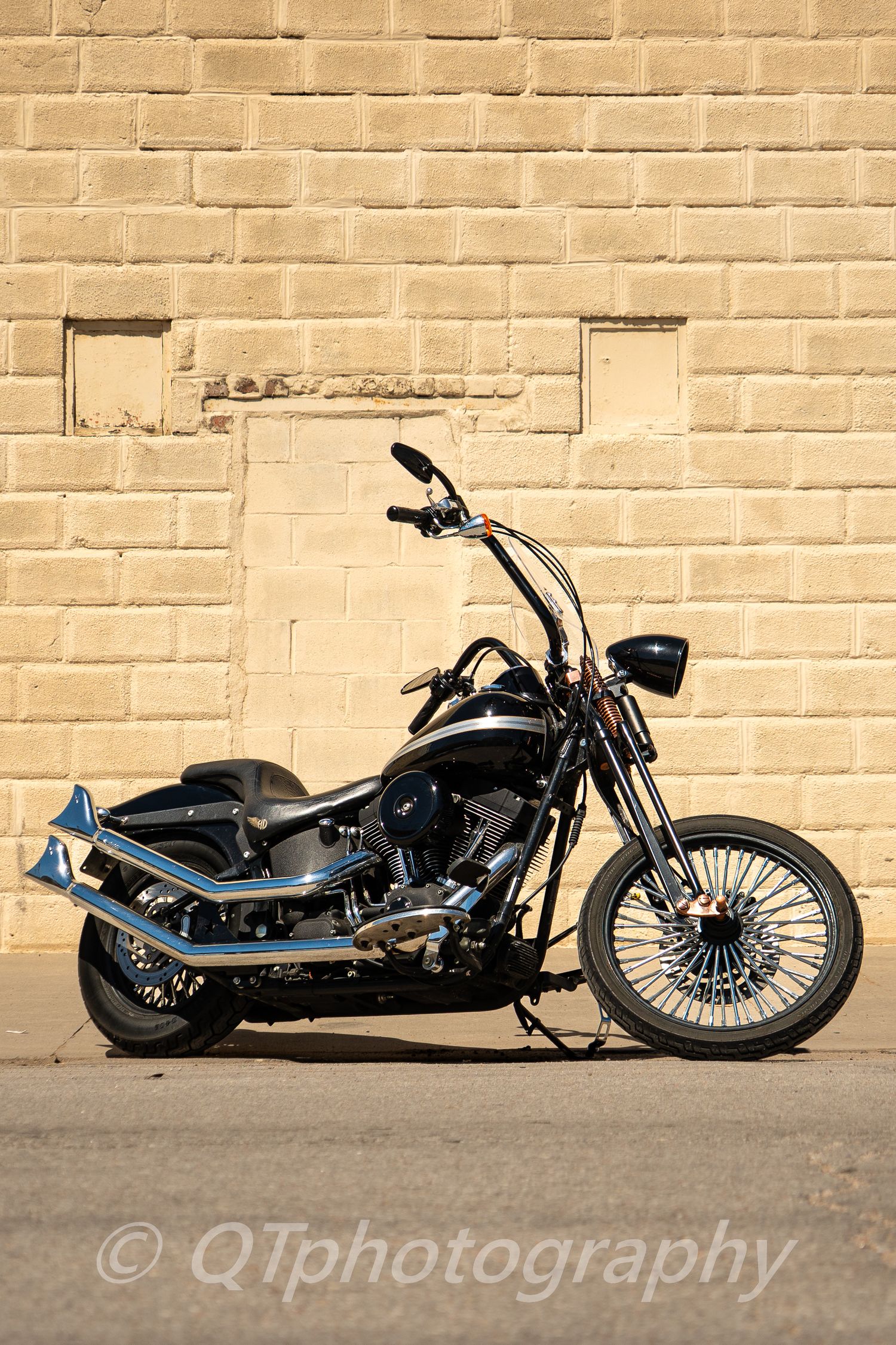 Custom motorcycle displayed against a beige brick wall in warm natural lighting.