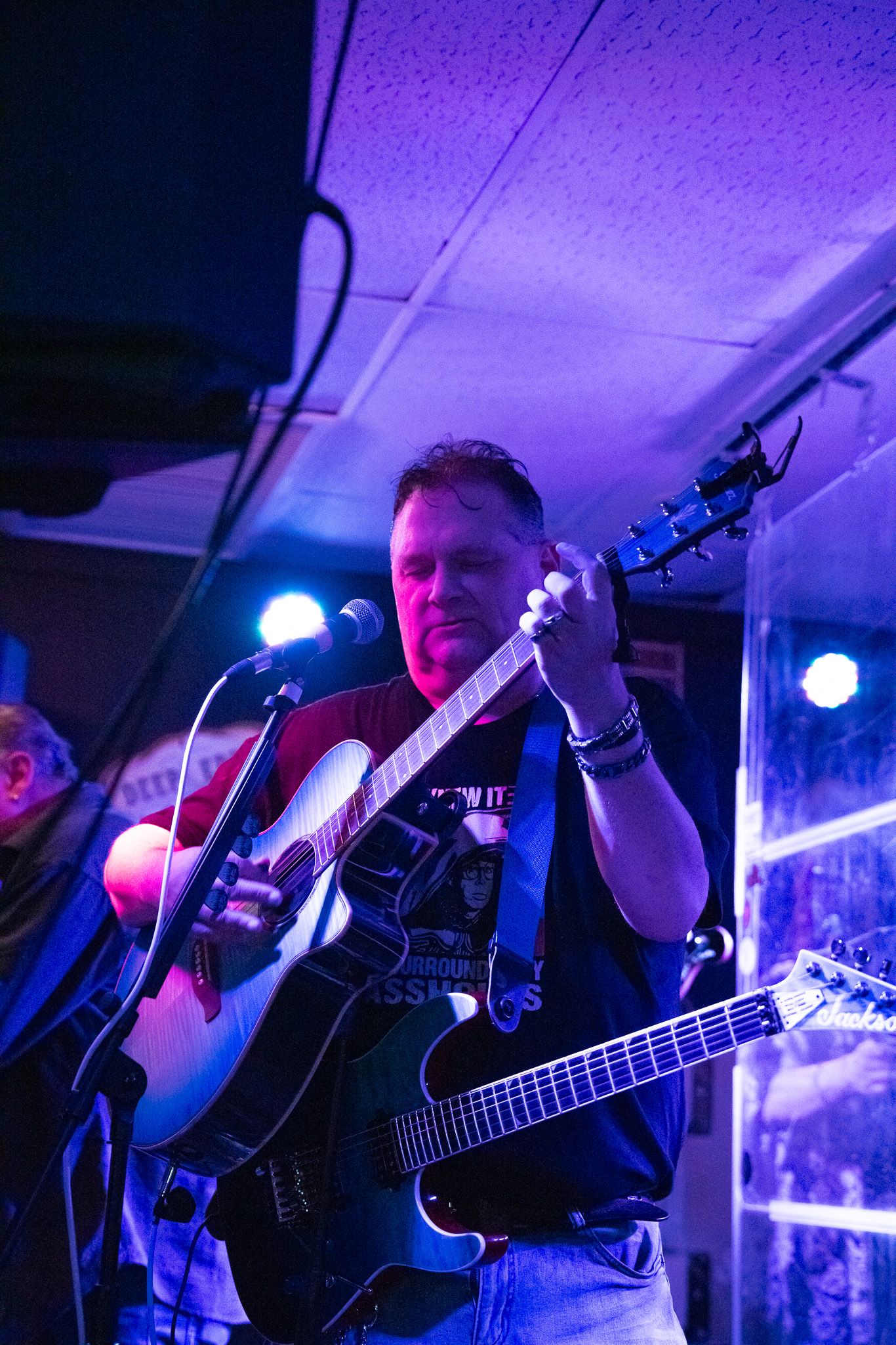 Musicians play instruments during a nightclub performance with purple stage lighting.