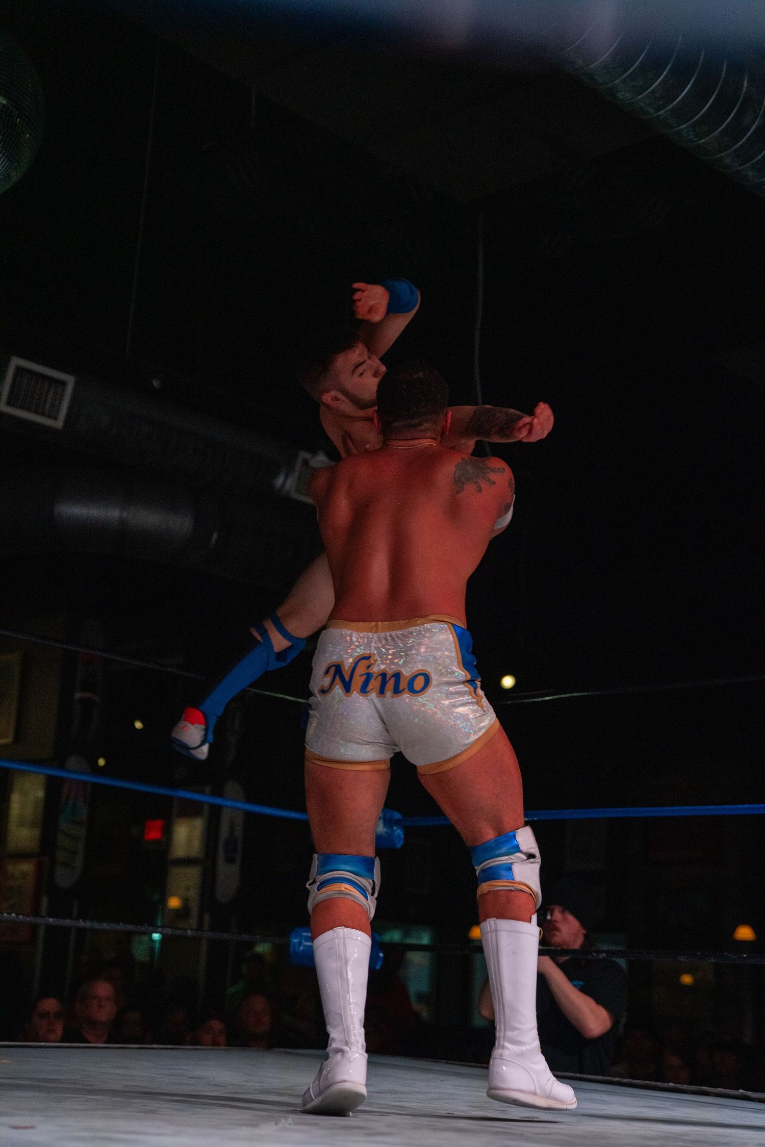 Professional wrestlers in white boots perform in a wrestling ring under bright lights.