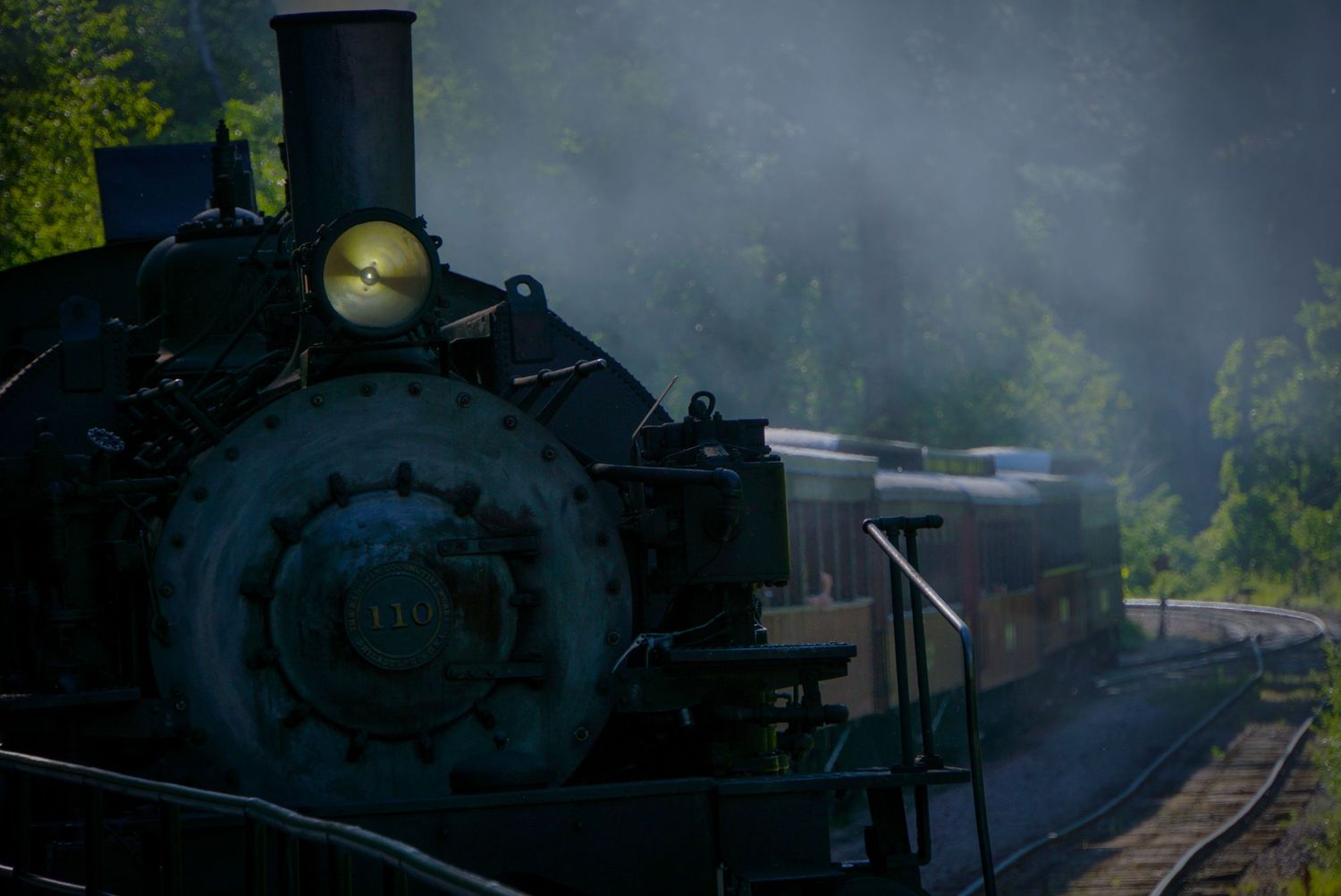Steam locomotive emerges through atmospheric fog on railway tracks.