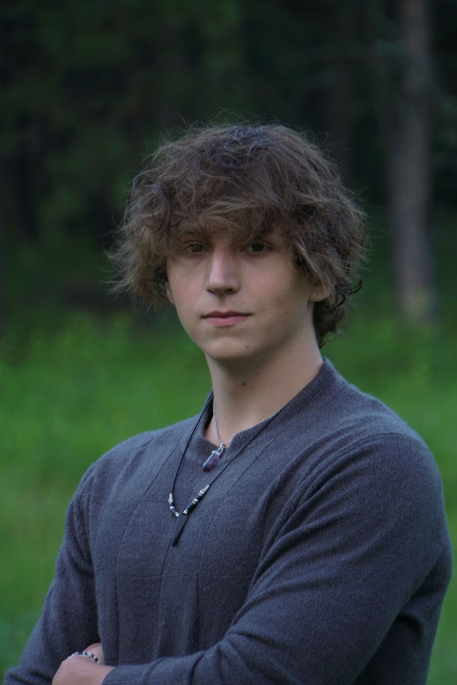 Person wearing a dark sweater poses against a blurred forest background in a moody portrait series.
