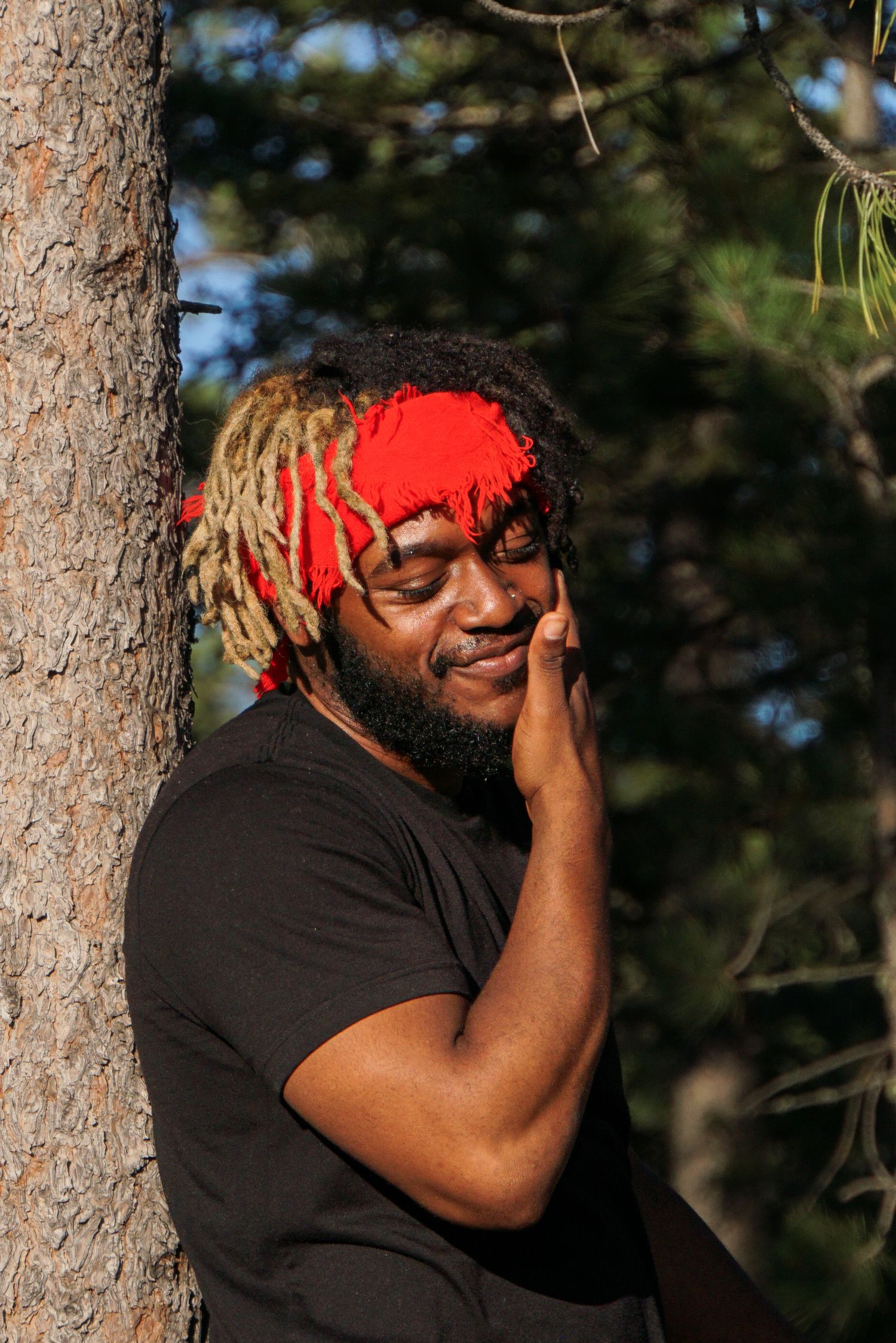 Person wearing red headwear poses thoughtfully in natural outdoor setting.