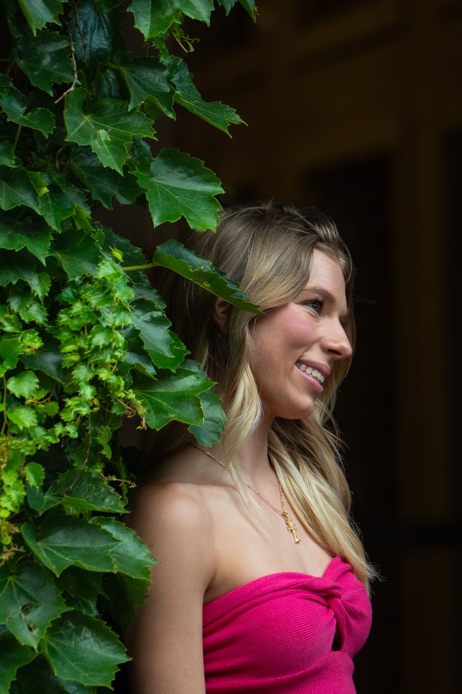 Portrait among green ivy leaves wearing bright pink top.