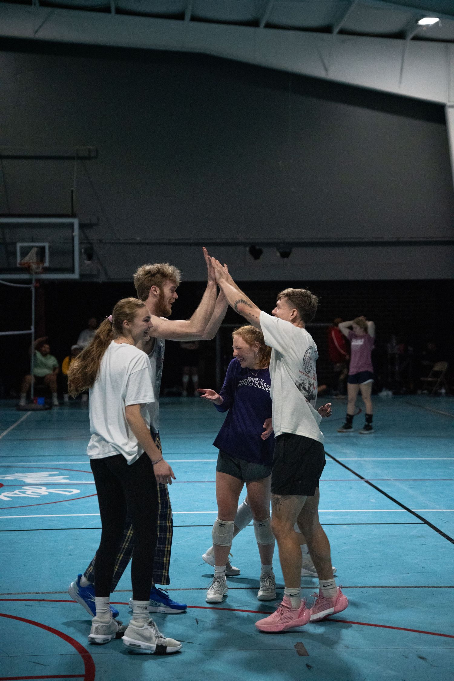 Players high-five each other during a volleyball game in a blue-floored indoor gymnasium.