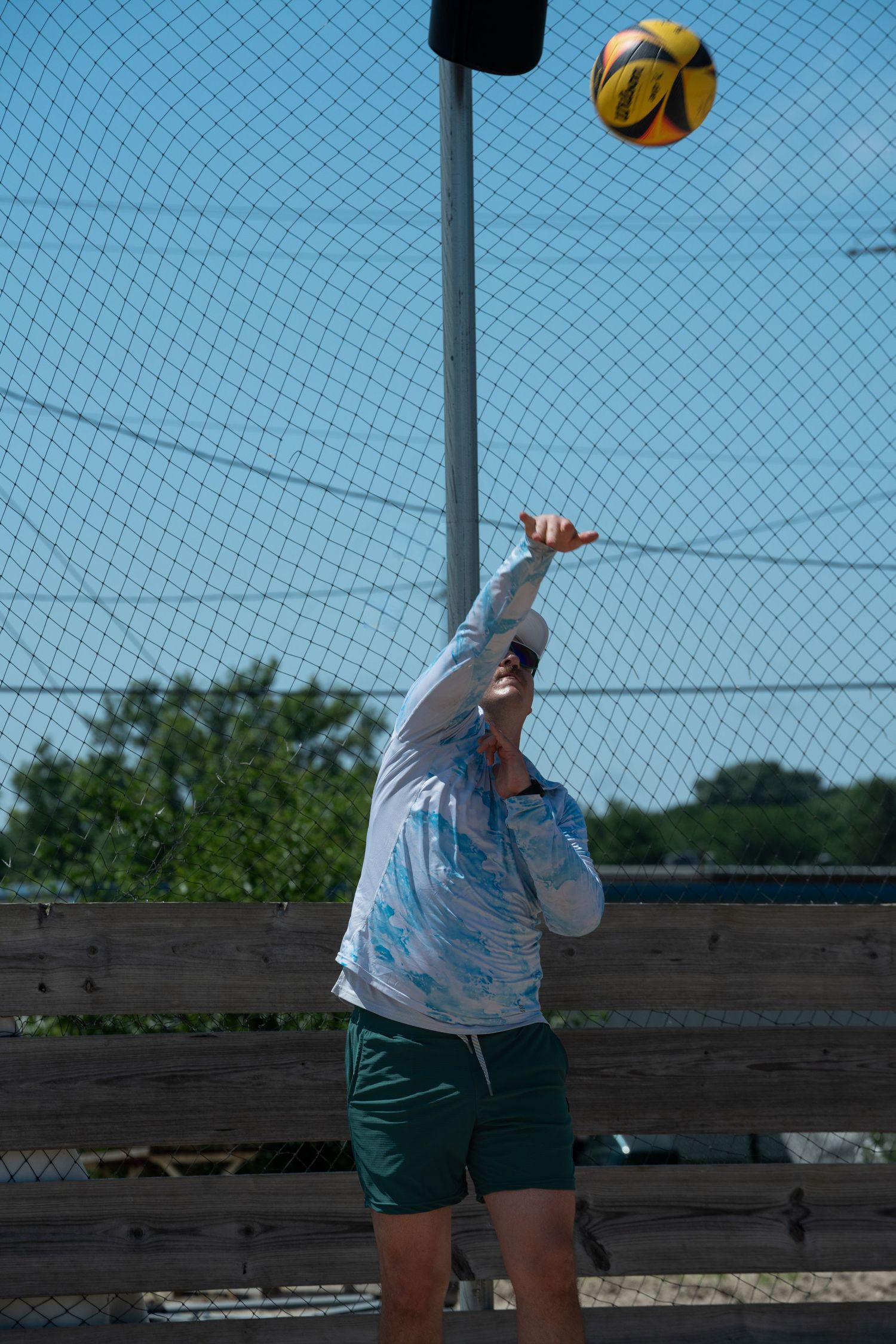 A sequence showing a beach volleyball player serving the ball over a net on a sunny day.
