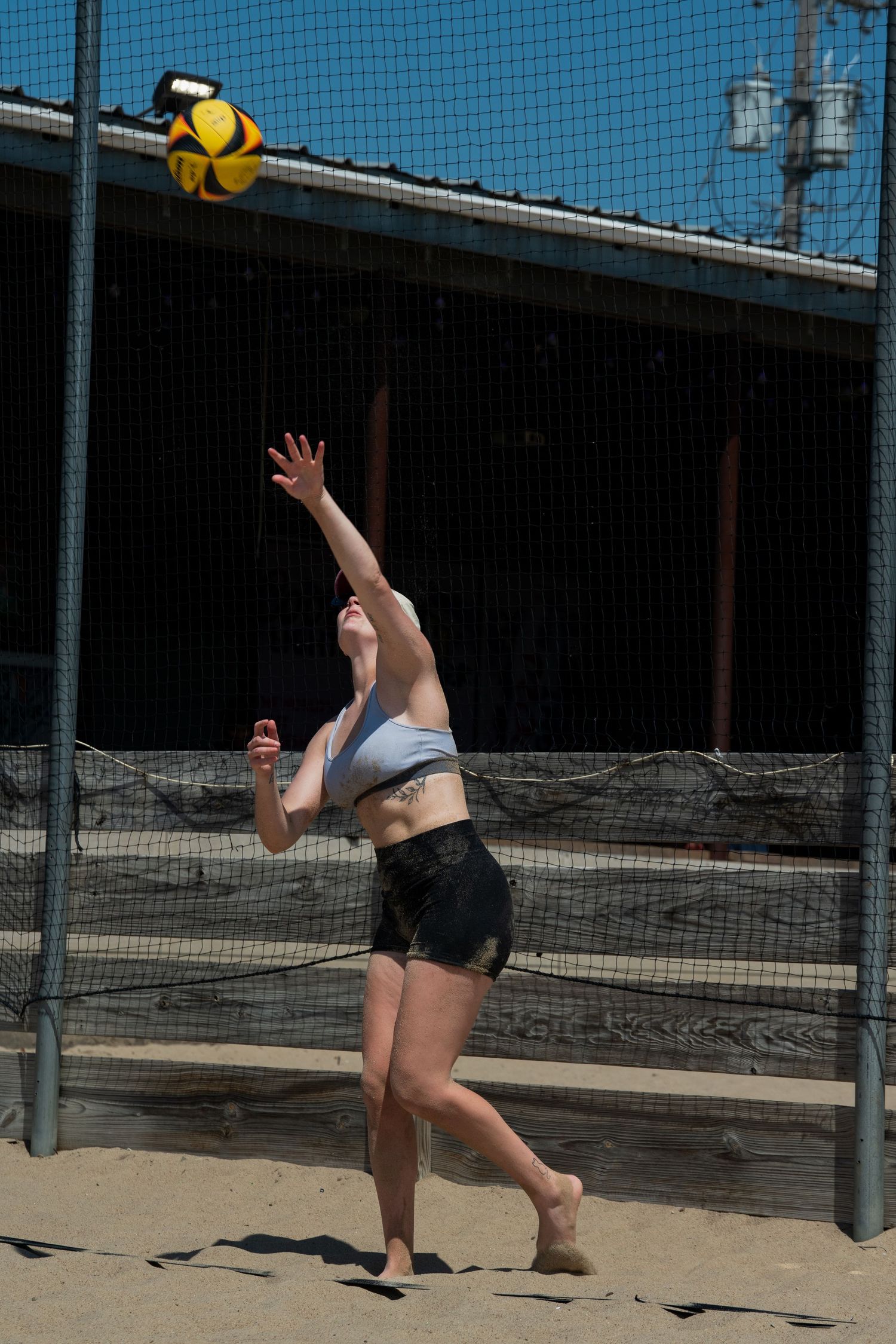 Beach volleyball player diving to save the ball on sandy outdoor court.