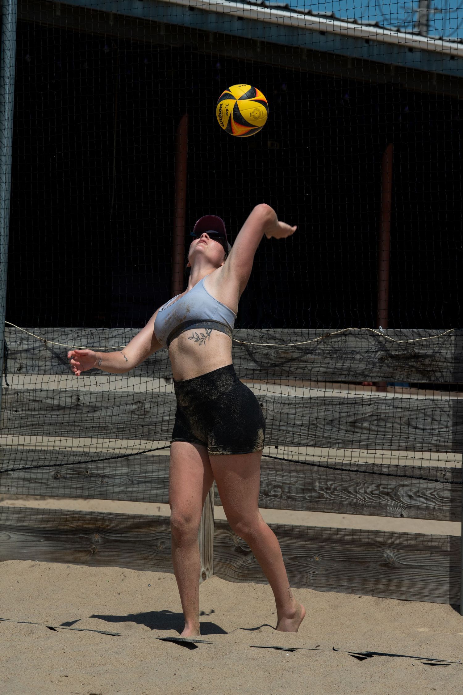 Player in athletic wear preparing to hit a yellow volleyball on sandy court.