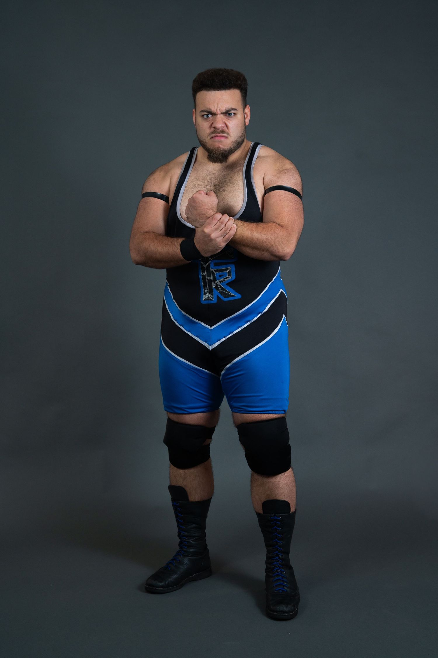 Professional wrestler in blue and black attire poses confidently in studio setting.