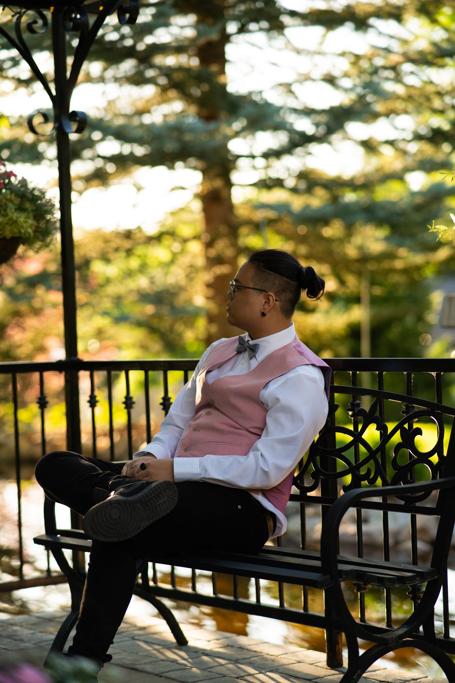 Person in formal attire relaxes on a black metal bench at sunset.