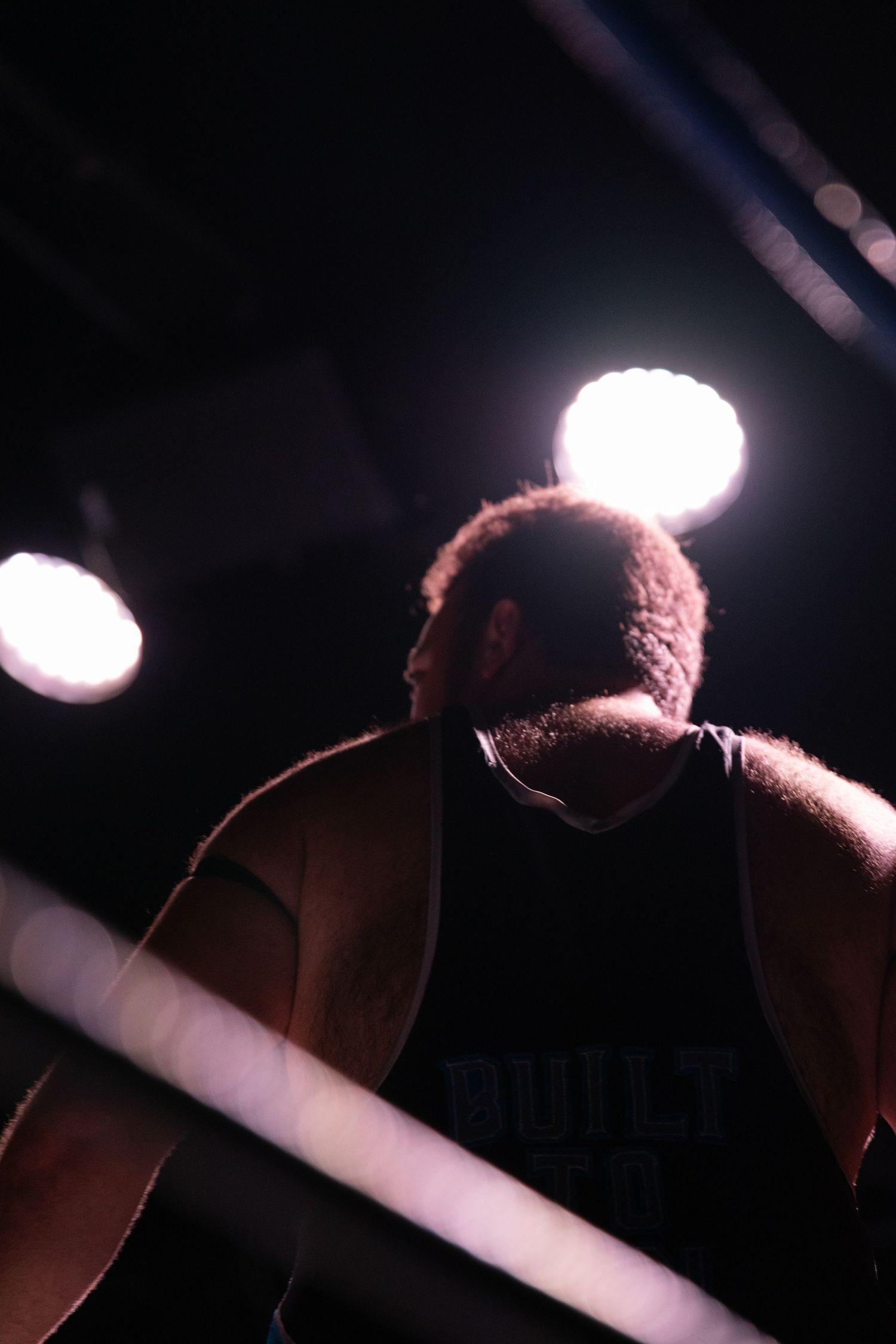 Silhouetted figure in a wrestling ring under dramatic spotlights.
