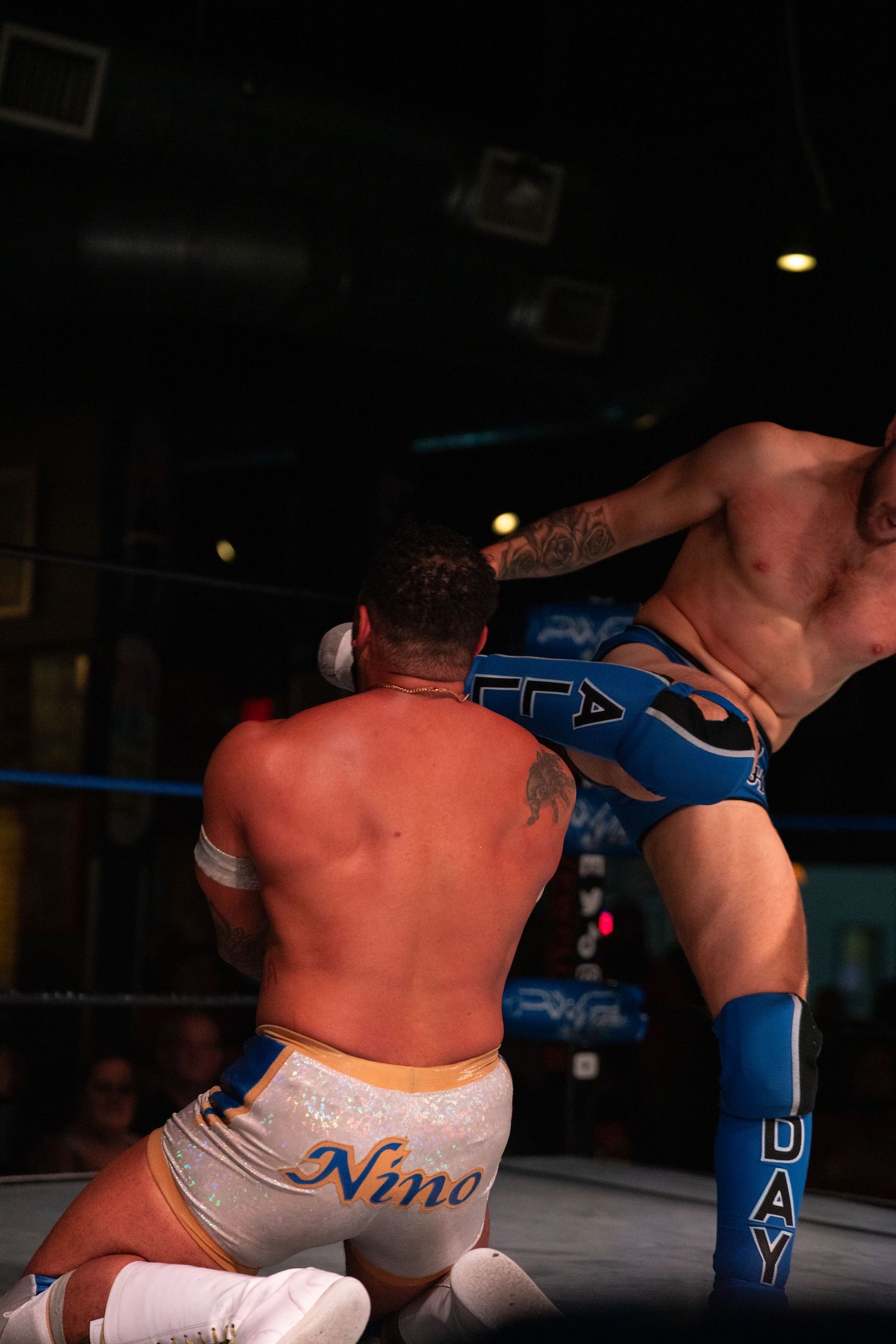 Two wrestlers grappling during an intense match on the mat in dramatic lighting.