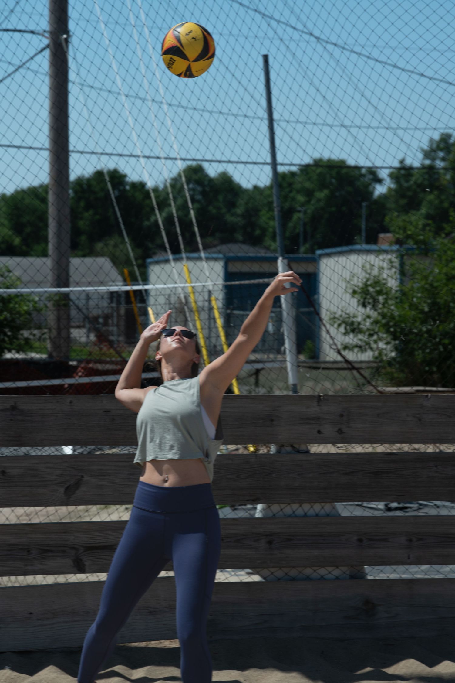 Player practicing volleyball serves on an outdoor court with chain link fence.