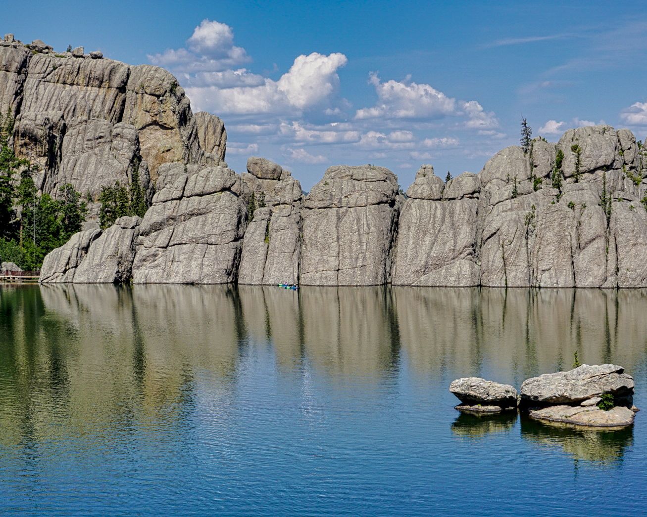 Panoramic view of rocky cliffs reflecting in calm blue lake water.