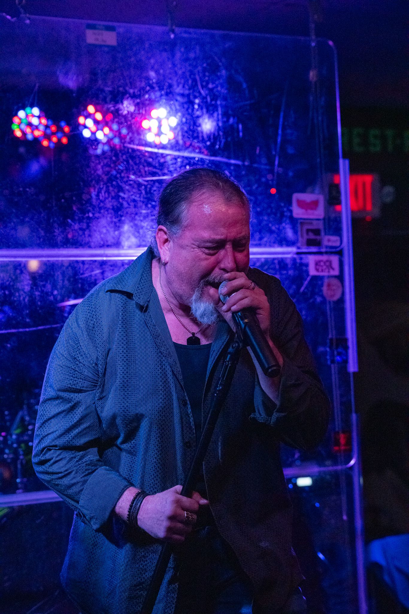 Performer sings into microphone on stage with blue and purple ambient lighting.